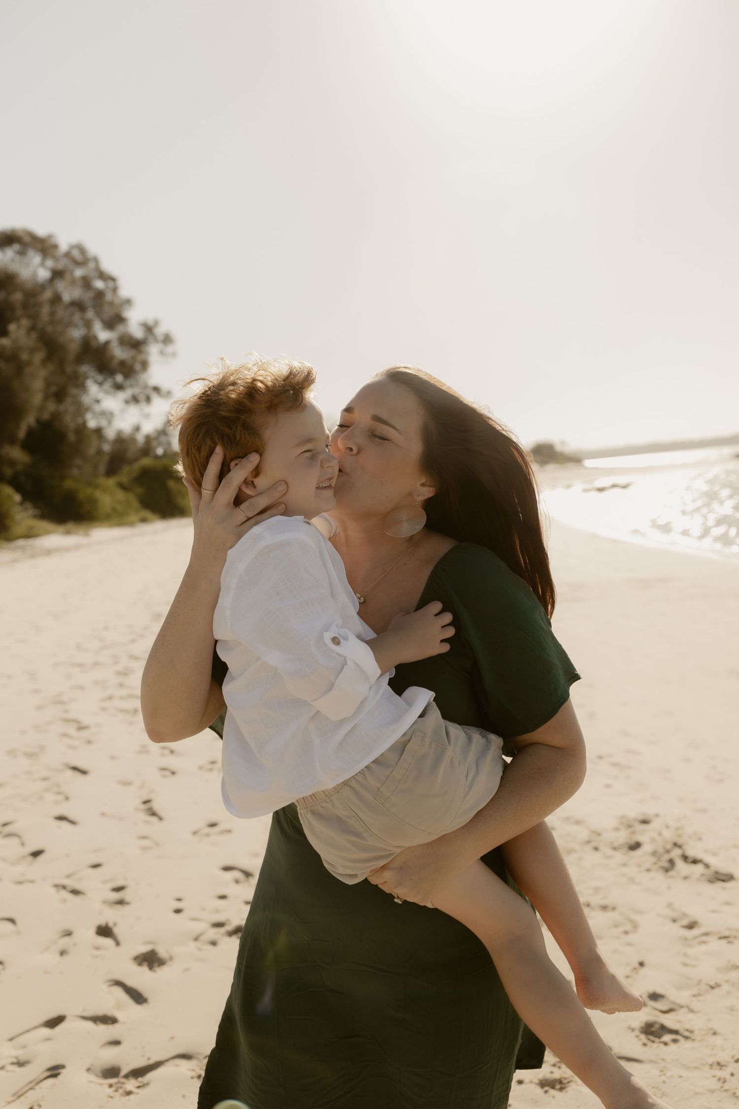 A tender moment between parent and child sharing a kiss on a sunlit beach.