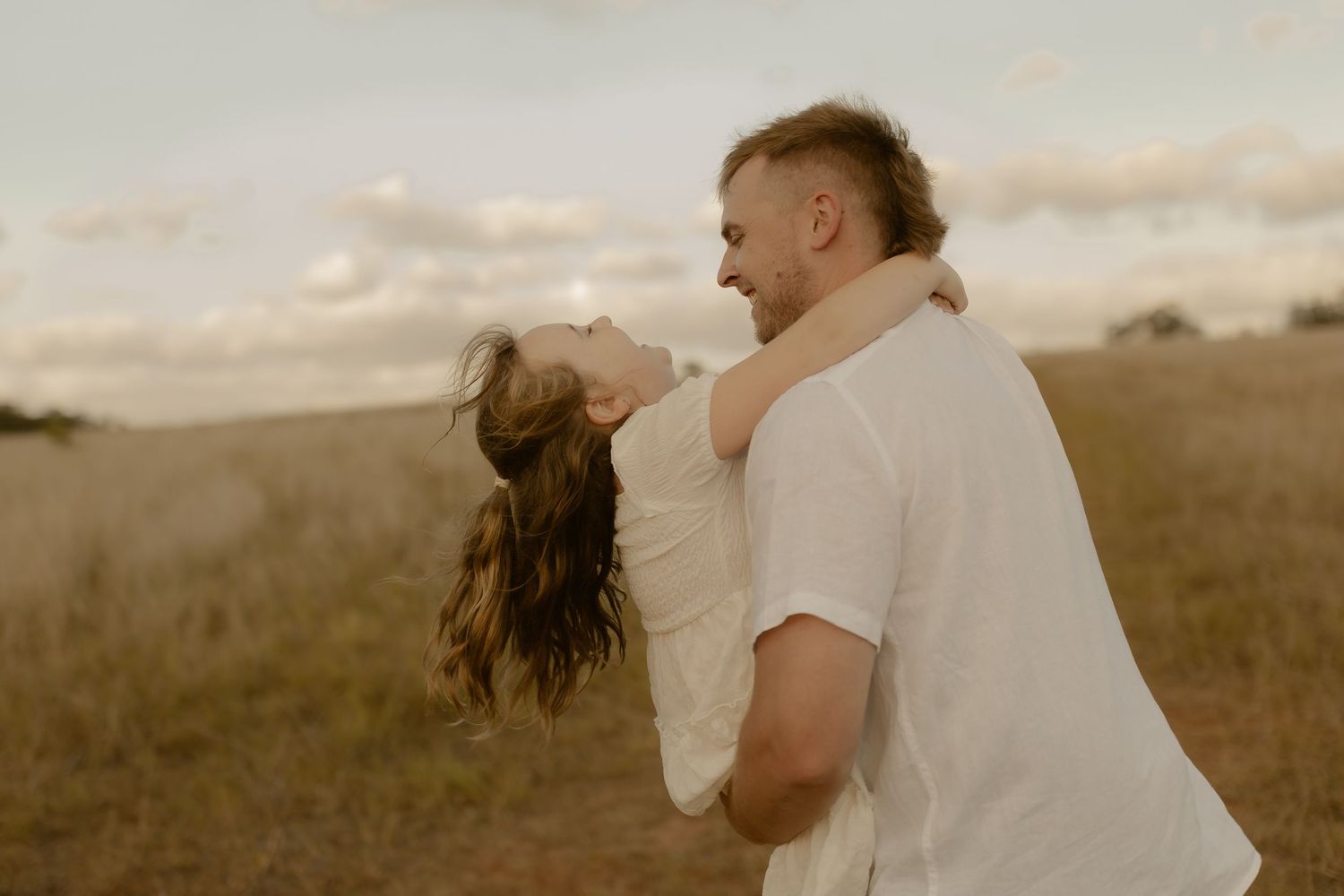 A couple embraces in a romantic moment on a hilltop during golden hour.