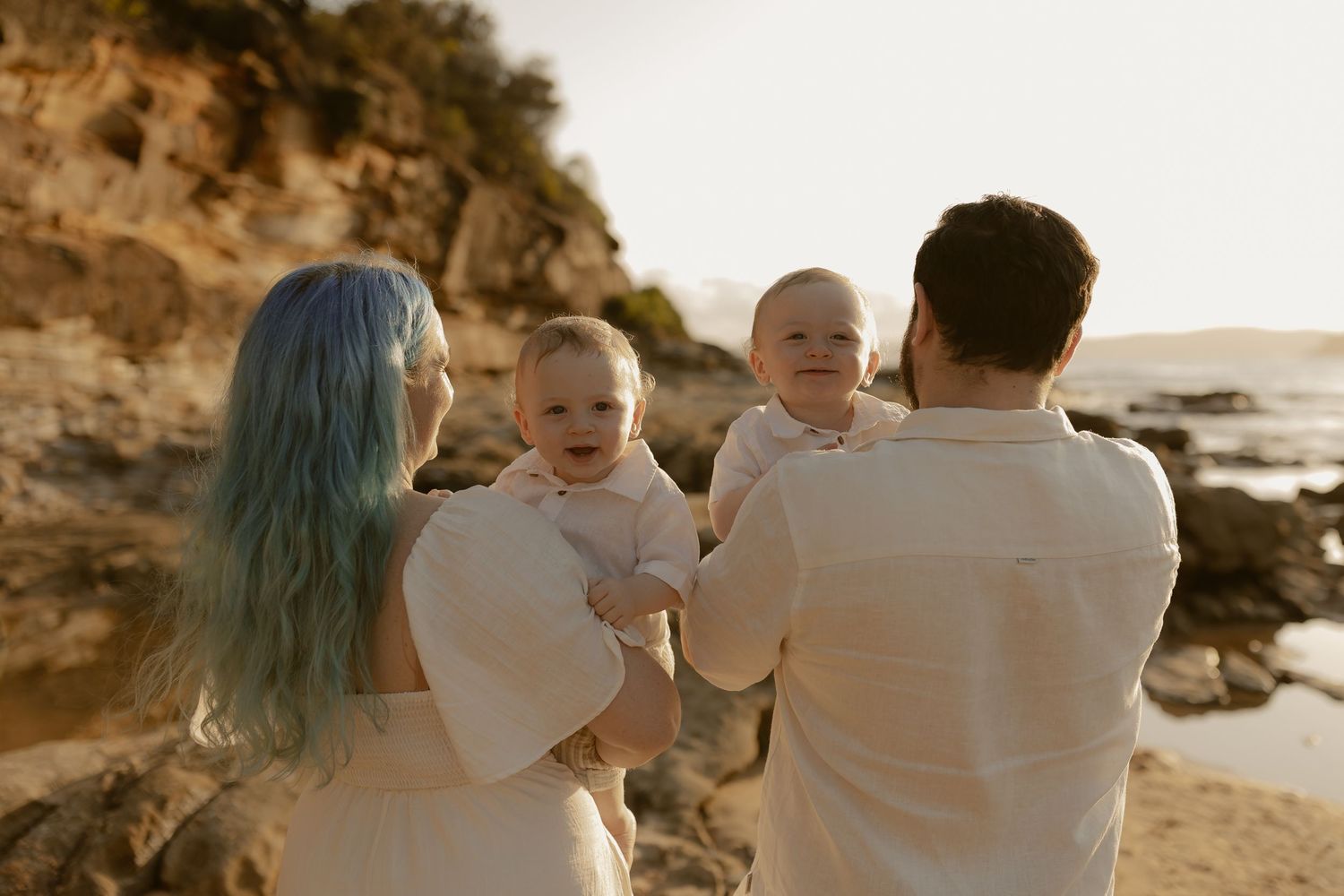 Family walking along rocky shoreline during golden hour photography session.