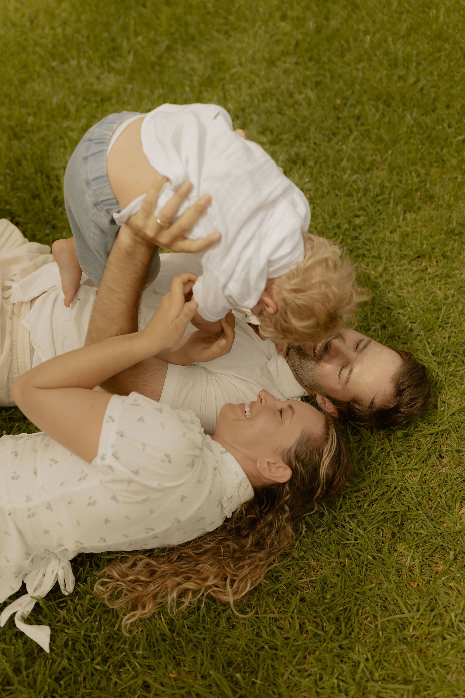 Two people lie together on green grass wearing white clothing.