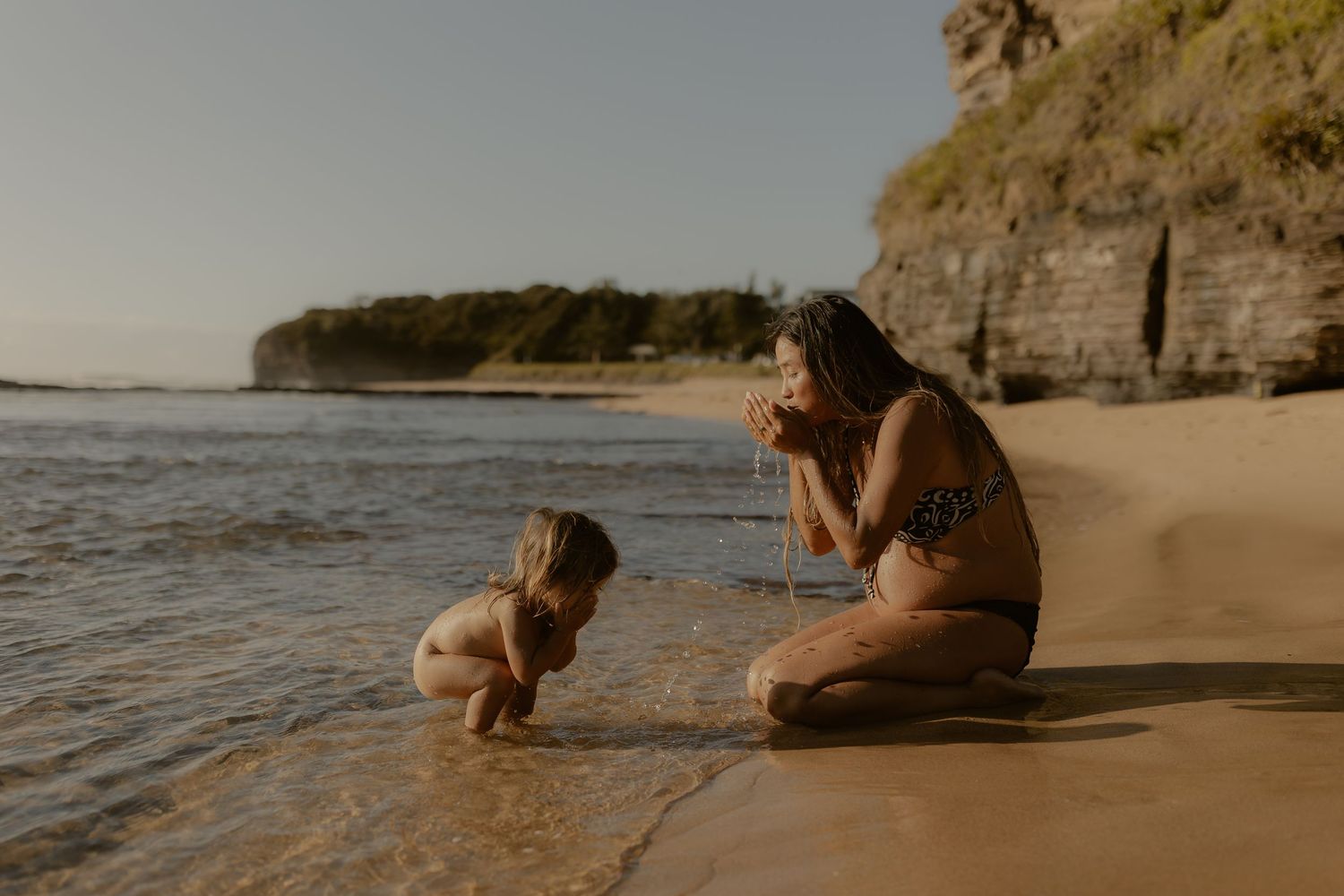 People lounging on a sandy beach with dramatic cliffs and ocean waves in the background.