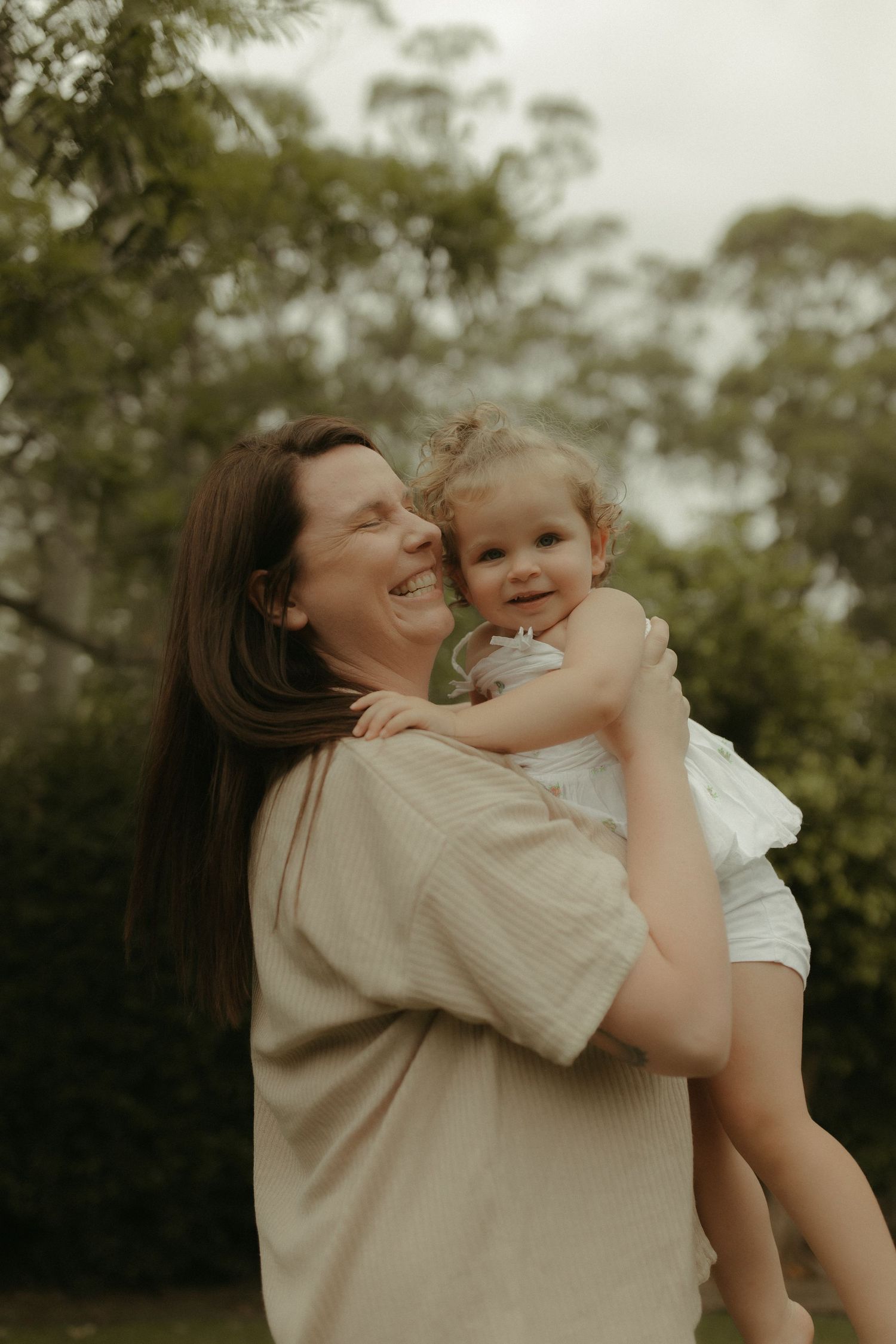 A joyful parent and child share a playful moment together outdoors with trees in the background.