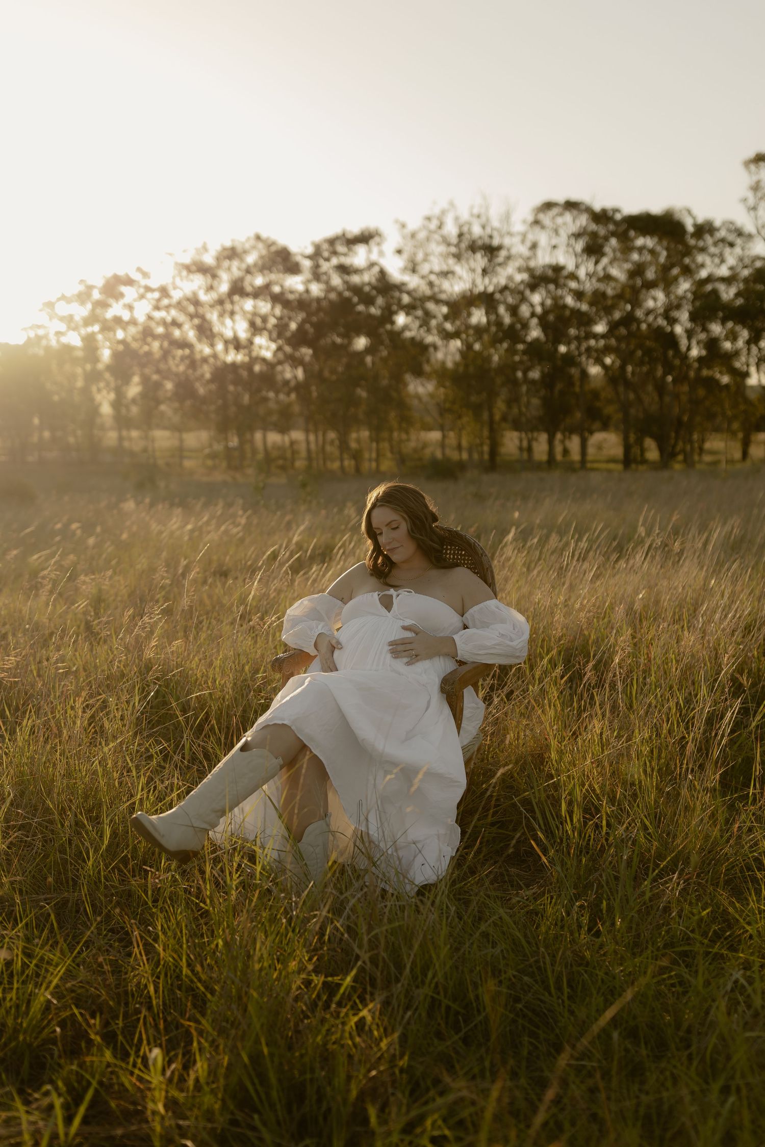 Person in flowing white dress lying peacefully in a sunlit meadow during golden hour.