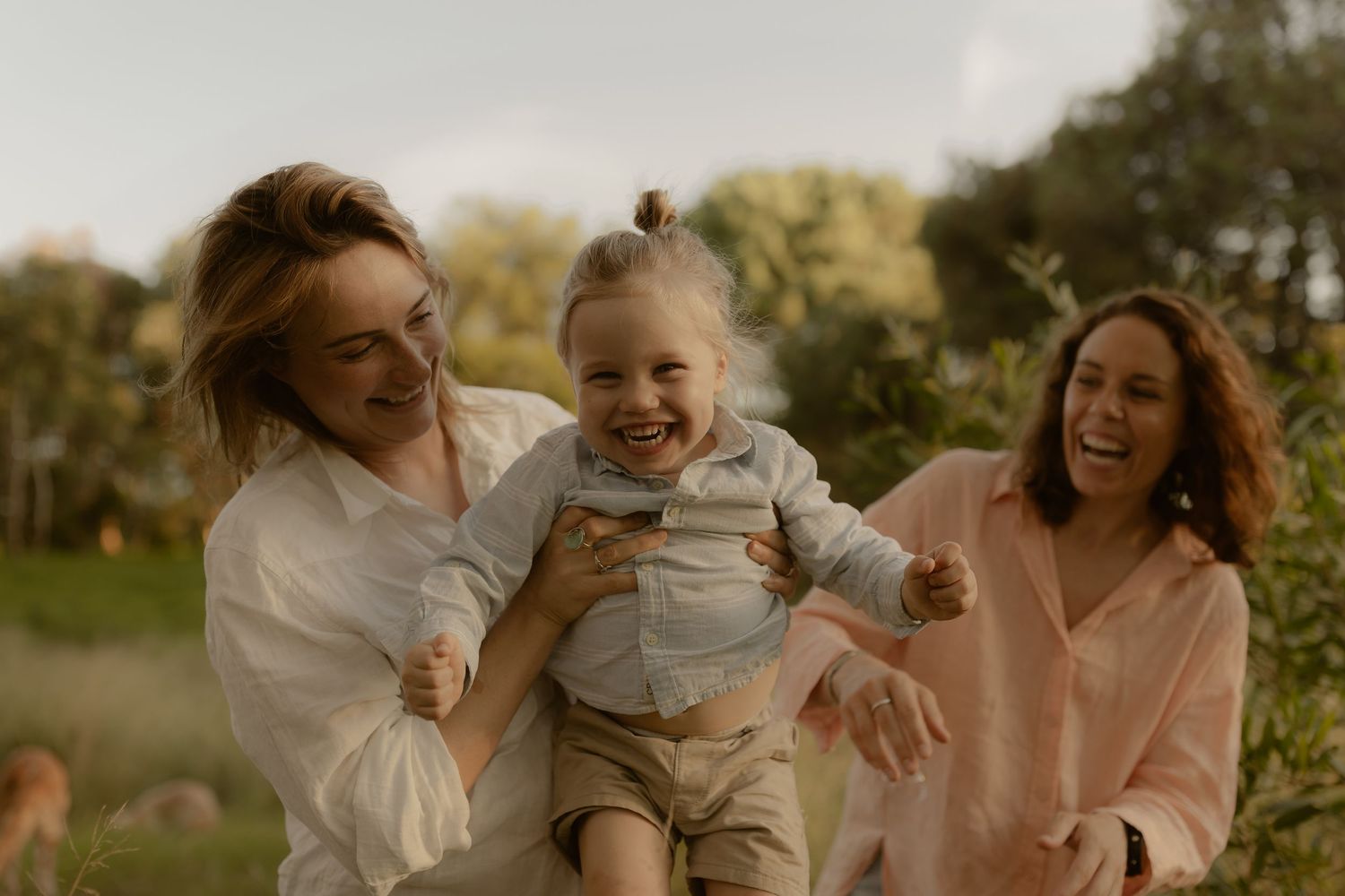 A joyful family moment captured outdoors during golden hour as they laugh and play together in a natural setting.