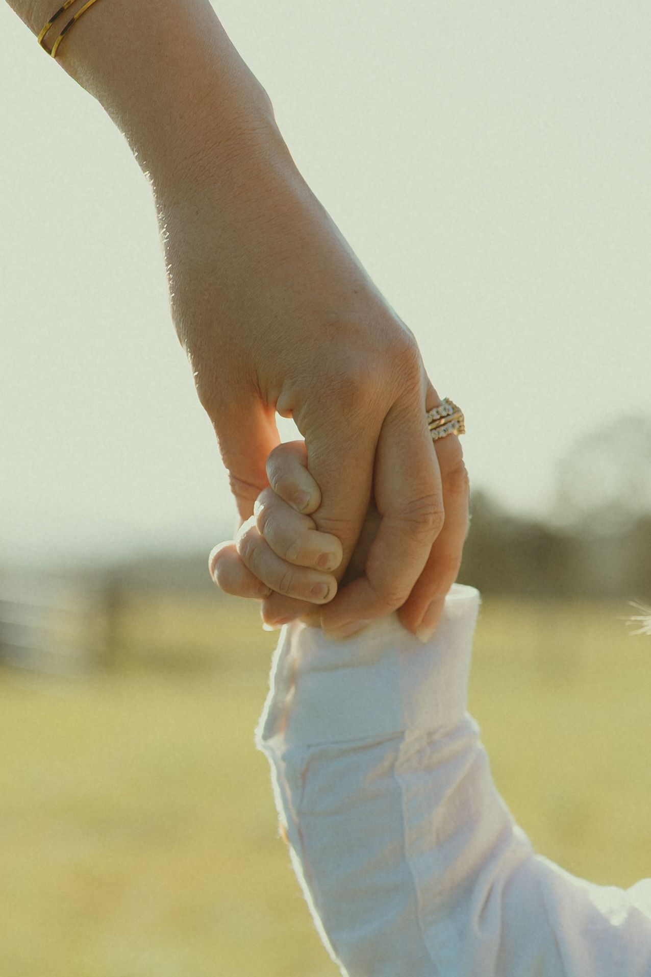 A close-up shot of hands clasped together against a sunlit rural background.