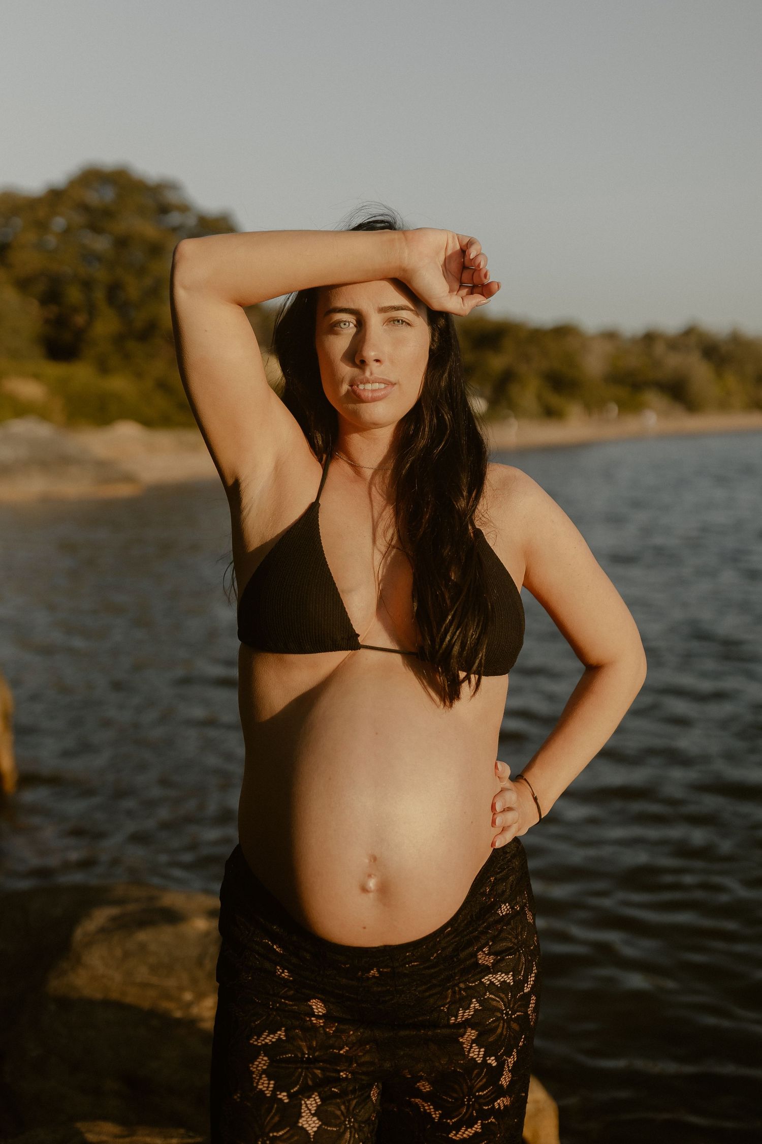 An intimate maternity photoshoot at the beach during golden hour showcases a black bikini and lace cover-up.