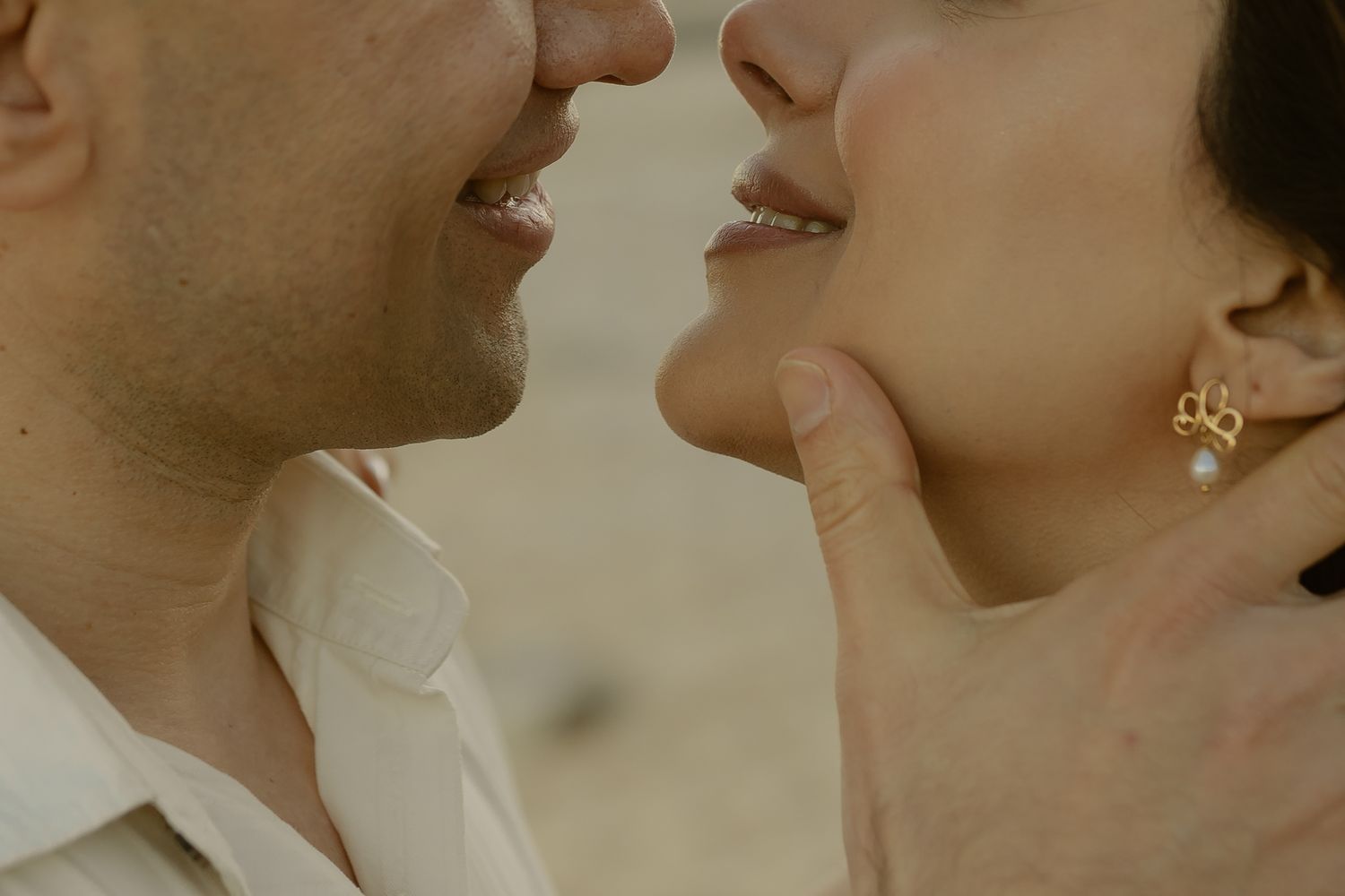 Close-up of a couple almost kissing, woman wearing gold pearl earrings, tender romantic moment.