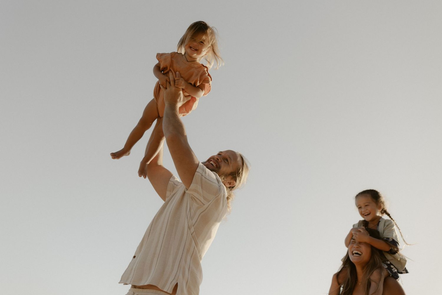 Family enjoying playful moments together against bright sky during sunset.