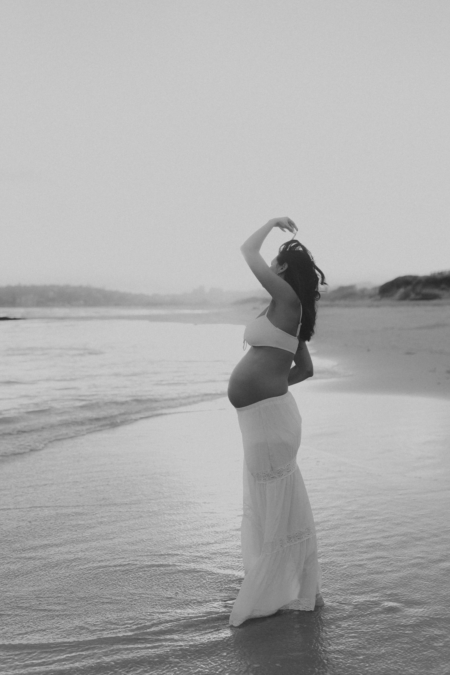 Ethereal black and white beach photography with flowing white dress against misty ocean backdrop.