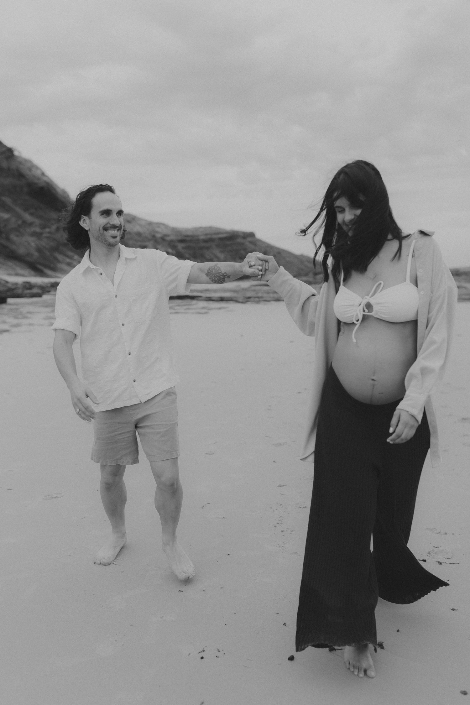 A couple walks together on a beach in black and white photography.