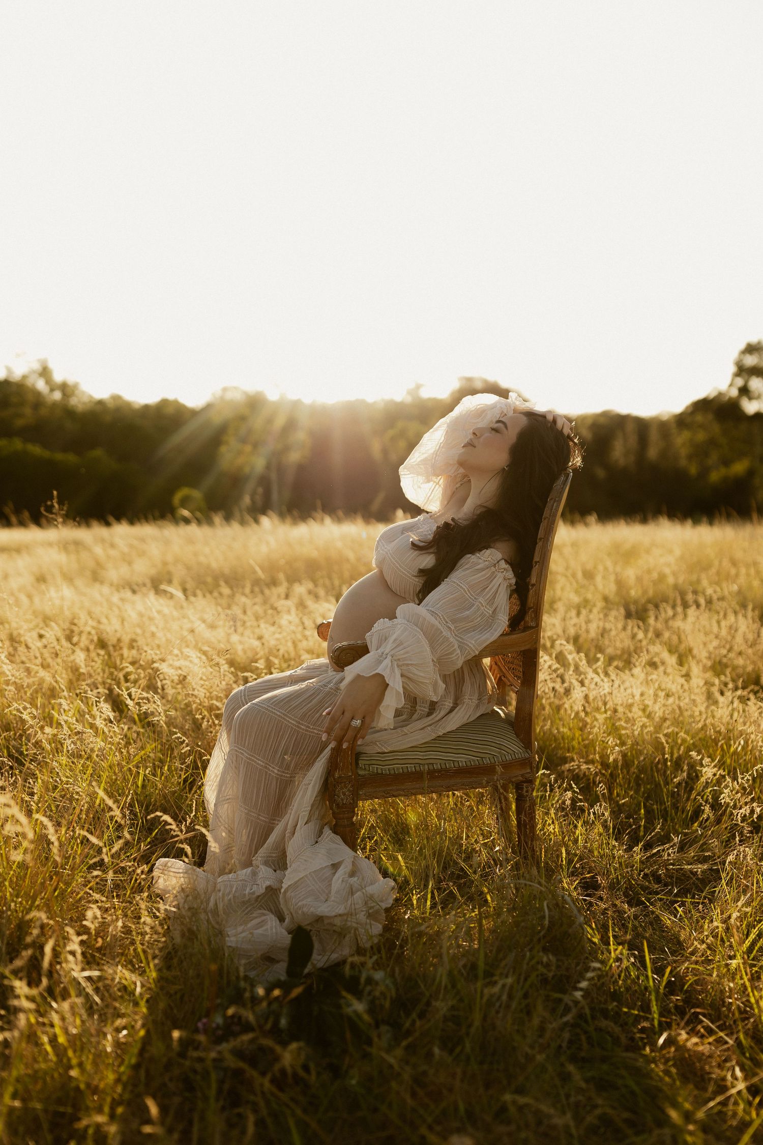 A couple relaxes in a vintage chair amidst a sun-drenched field during golden hour.