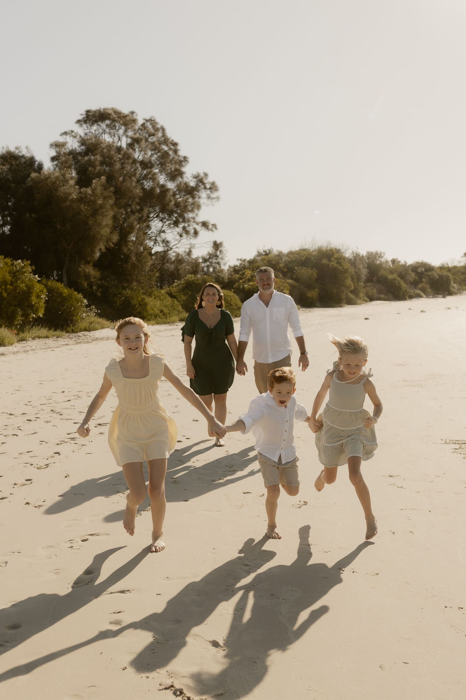 Family running together on sandy beach creating long shadows in evening light.
