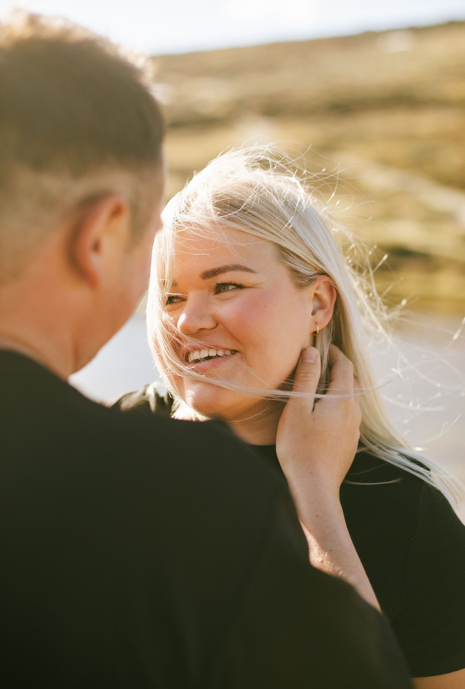 A couple shares an intimate moment in golden sunlight as blonde hair gently blows in the wind.