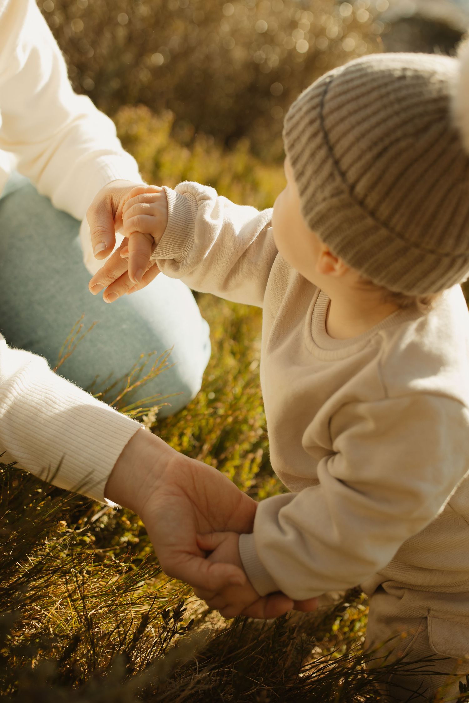 Small hands hold together tenderly in warm sunlit grass during an intimate outdoor moment.