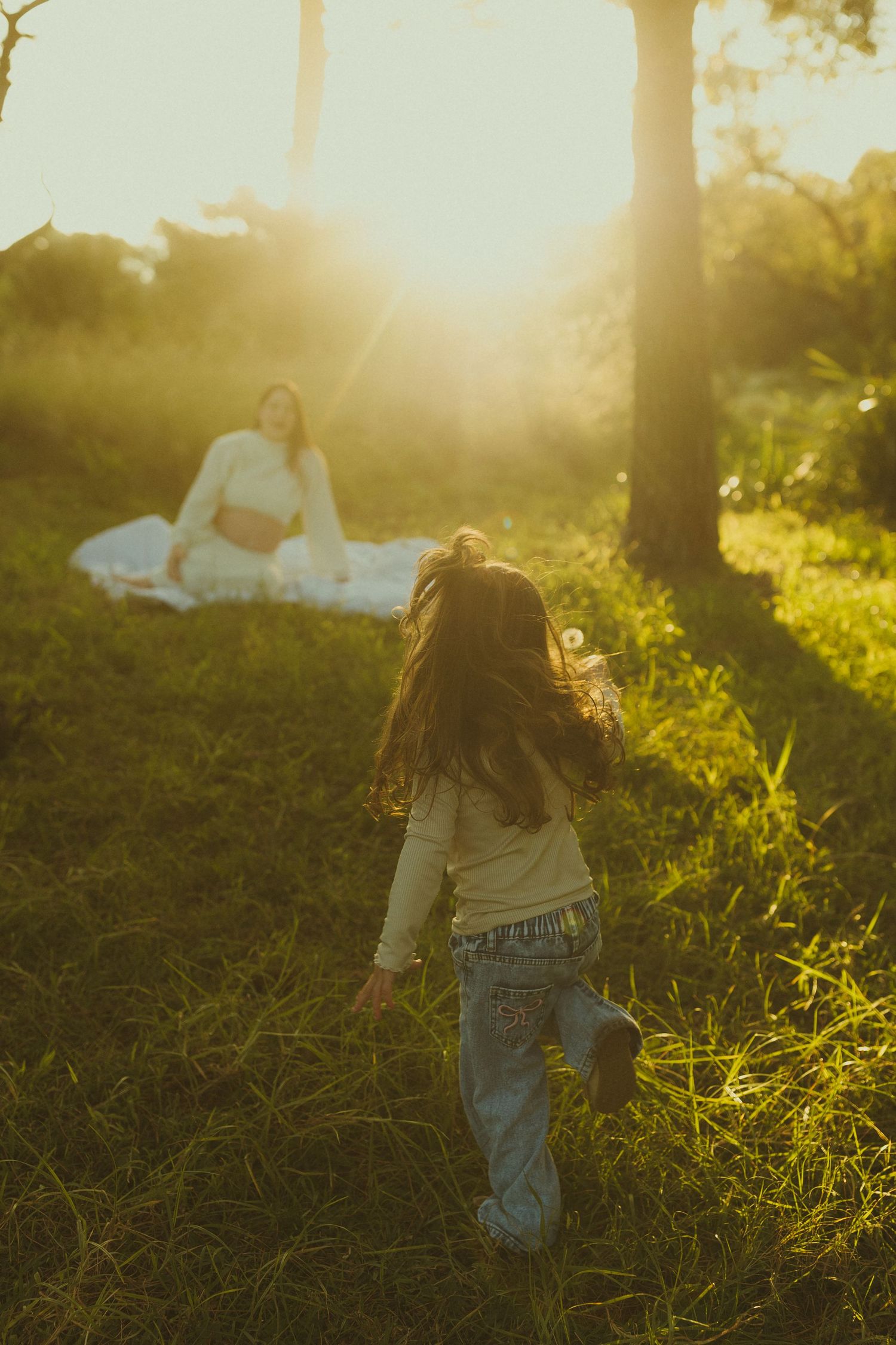 Person sitting on grass during golden hour with sunlight filtering through trees.