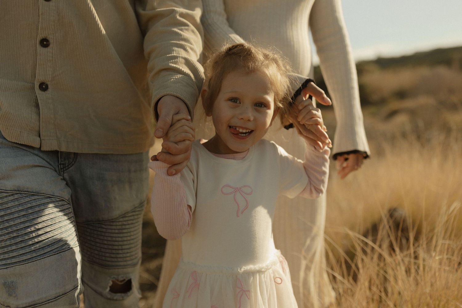 Candid moment of joy and laughter while holding hands in a sun-drenched field of tall grass.