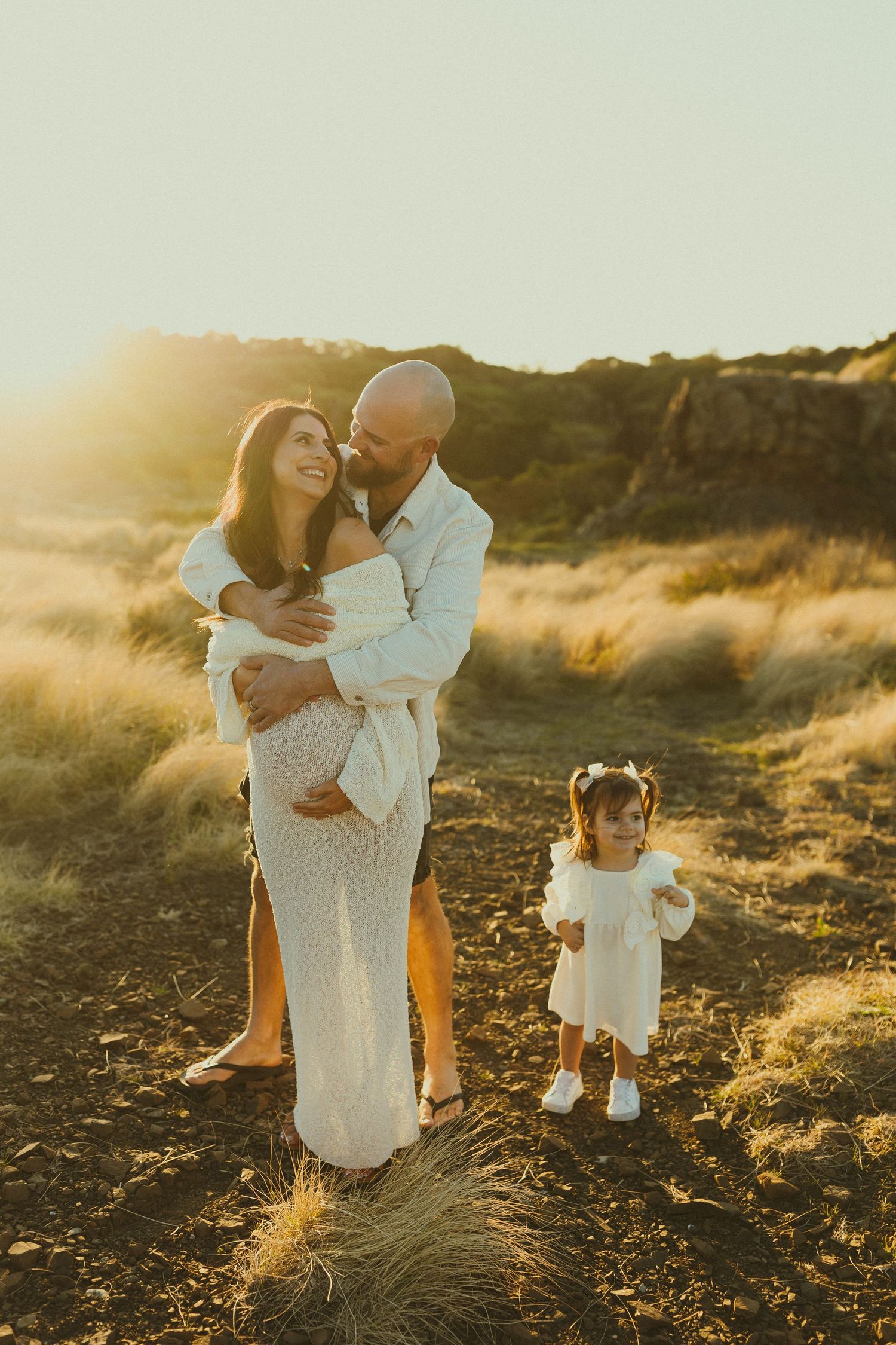 Candid family embracing in warm sunset light among desert brush and rocky terrain.