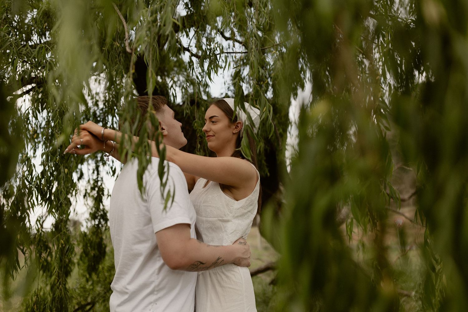 Couple dancing under willow tree branches in an outdoor setting.