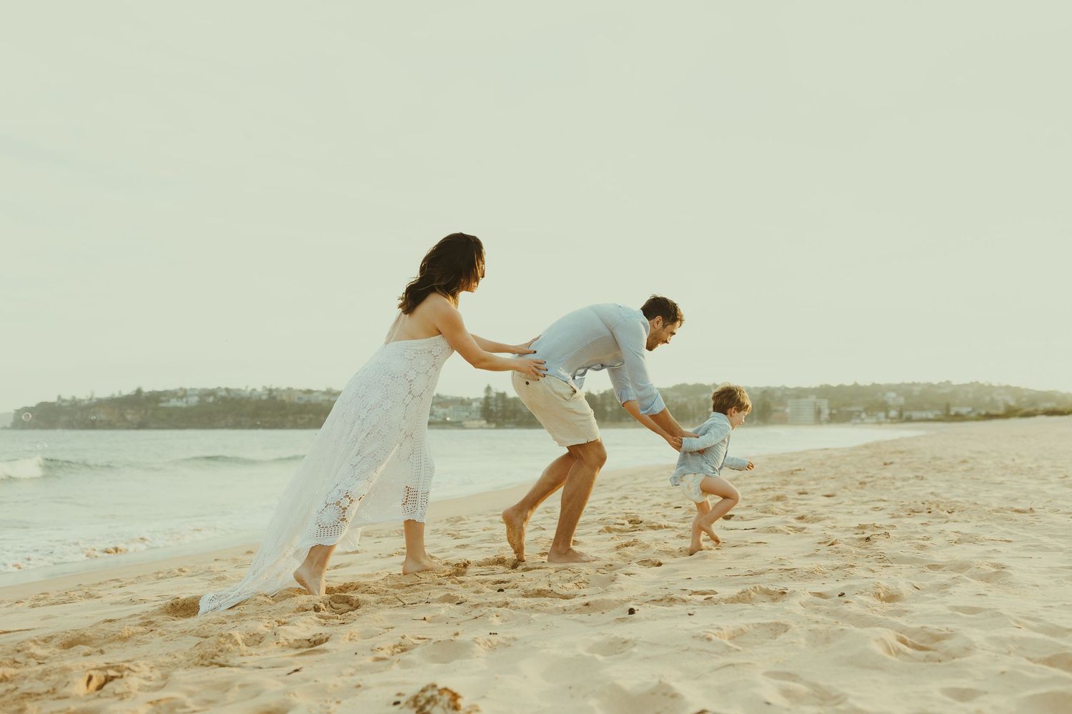 A family plays and runs together along the shoreline during golden hour.