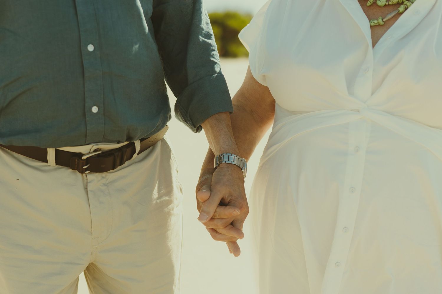 Close-up of couple holding hands on beach in casual wedding attire.