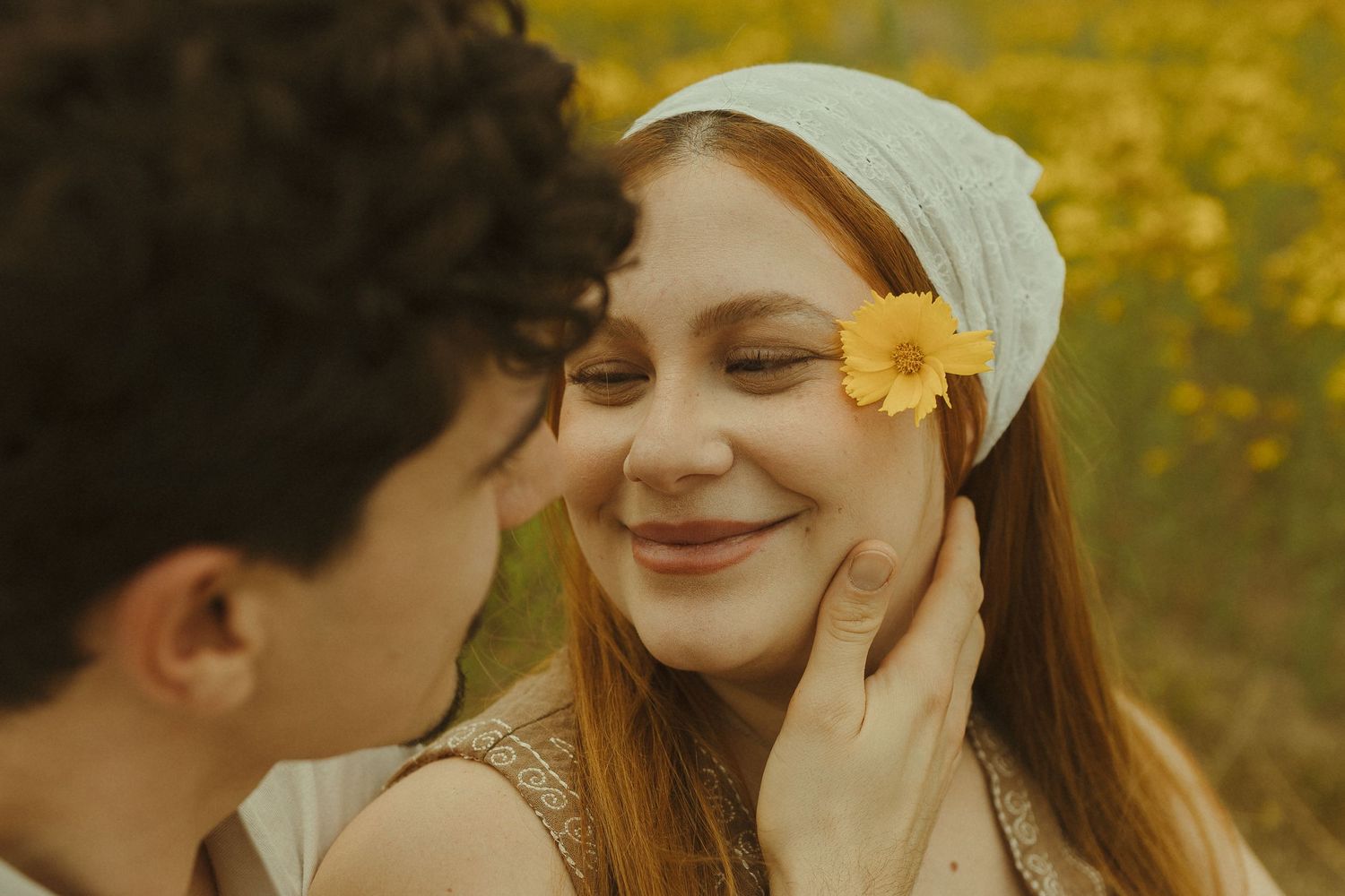 Romantic couple embraces in a field of vibrant yellow wildflowers during golden hour.