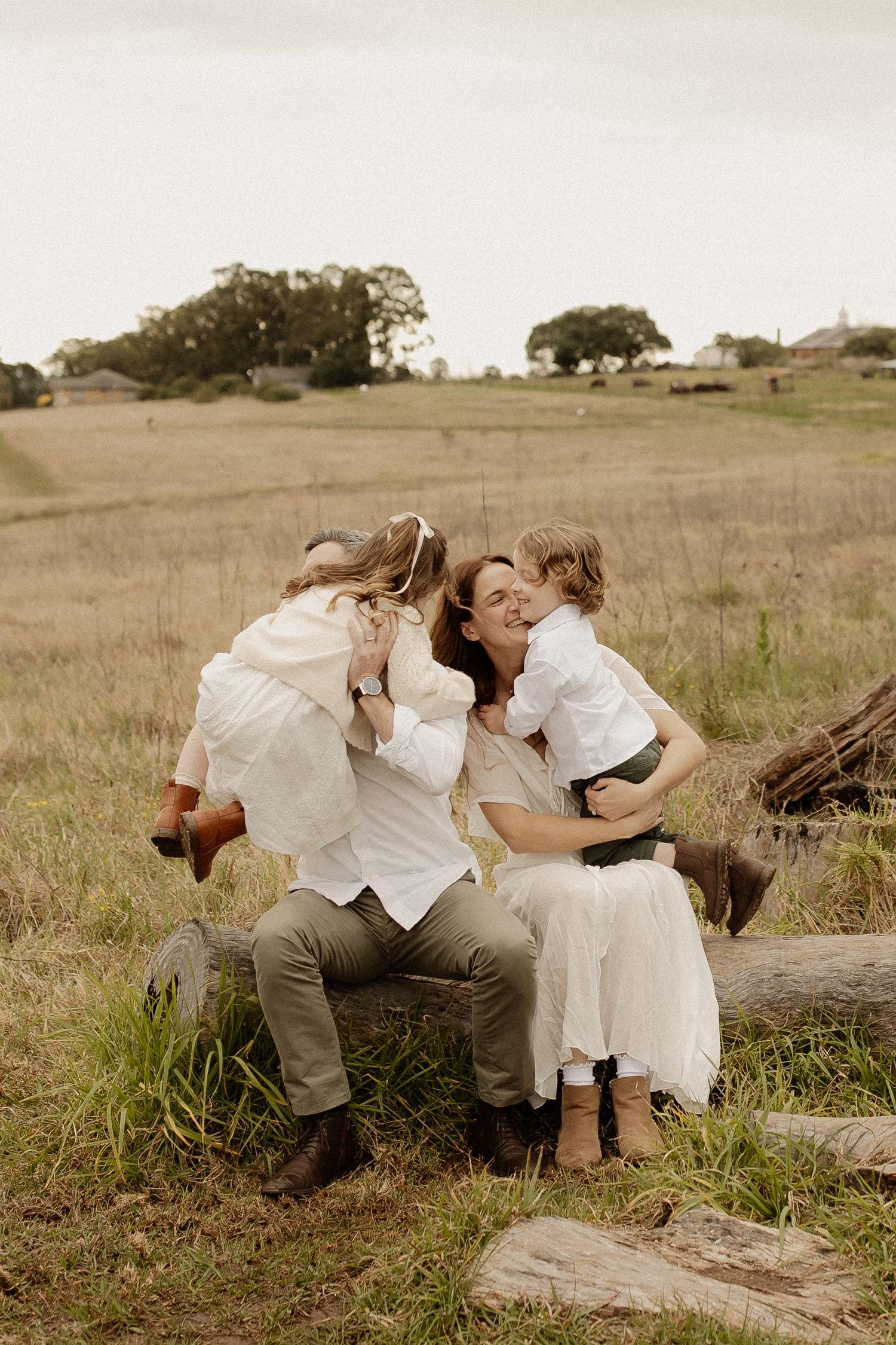 Couple in white and khaki outfits share intimate moments in a rustic outdoor setting with rolling hills.