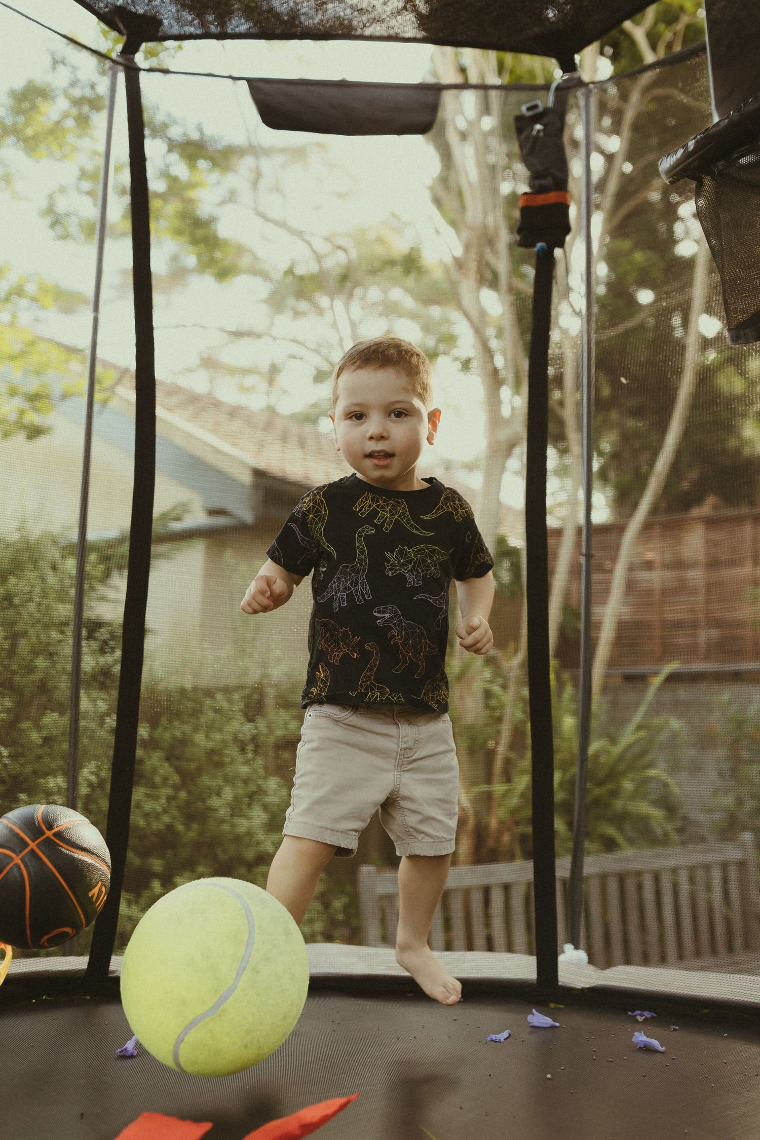 A child jumping and playing on a backyard trampoline with toys.