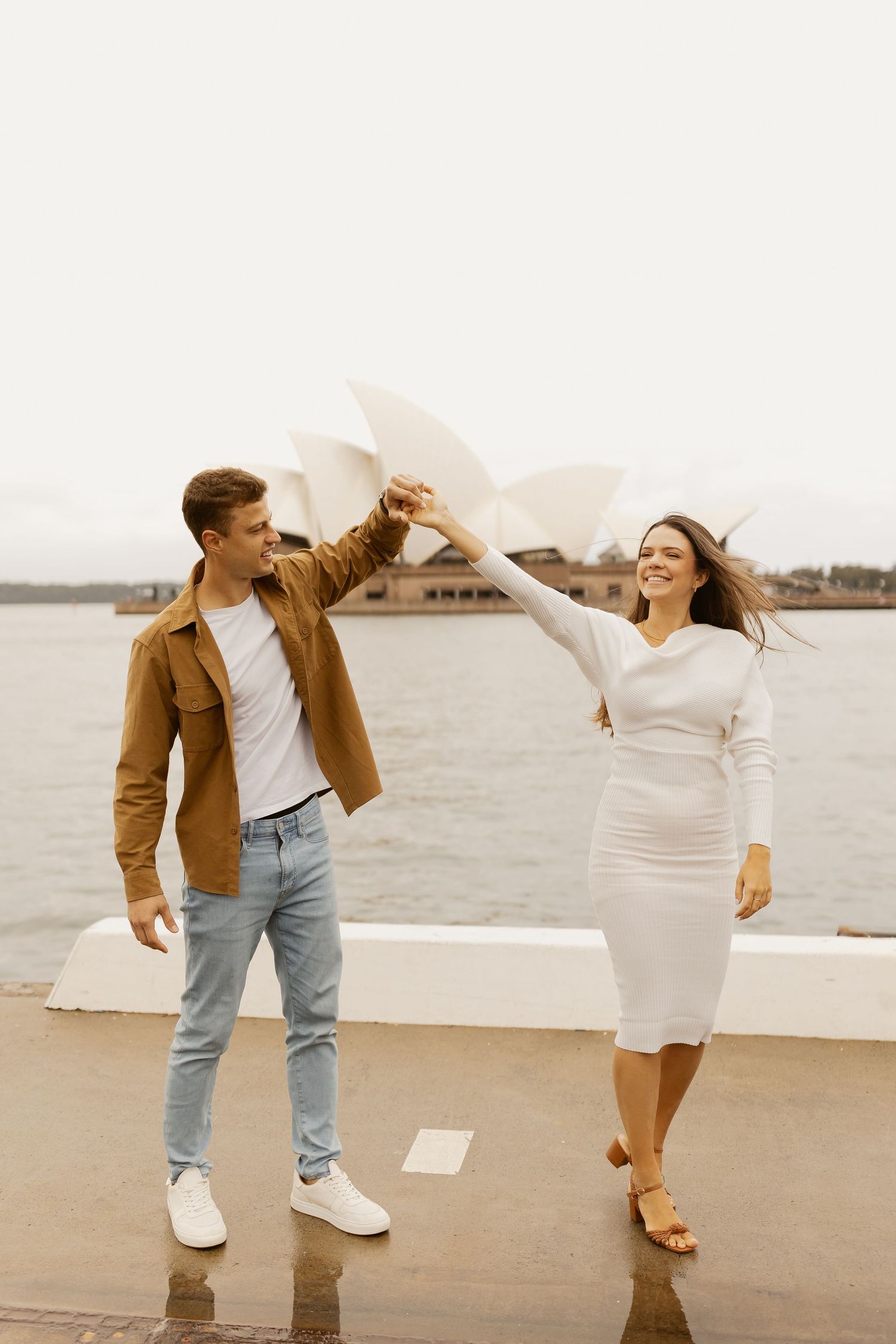 Couple dancing and twirling near Sydney Opera House in elegant attire.