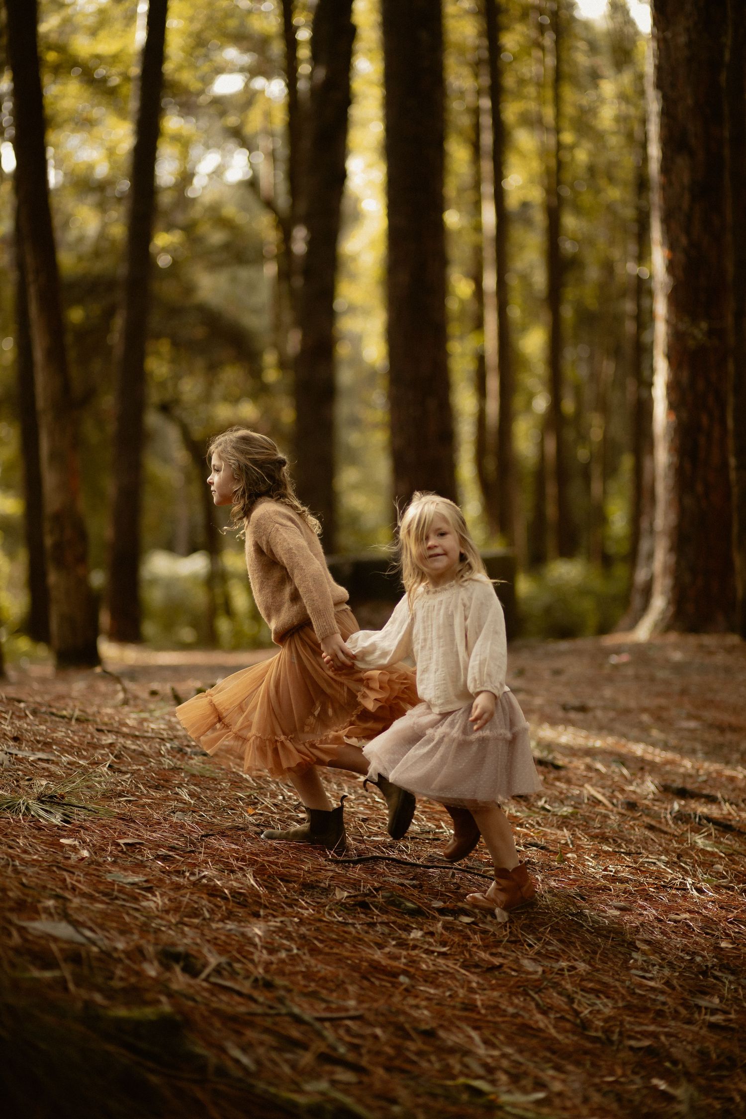 Two people dancing joyfully among tall trees in a forest setting.