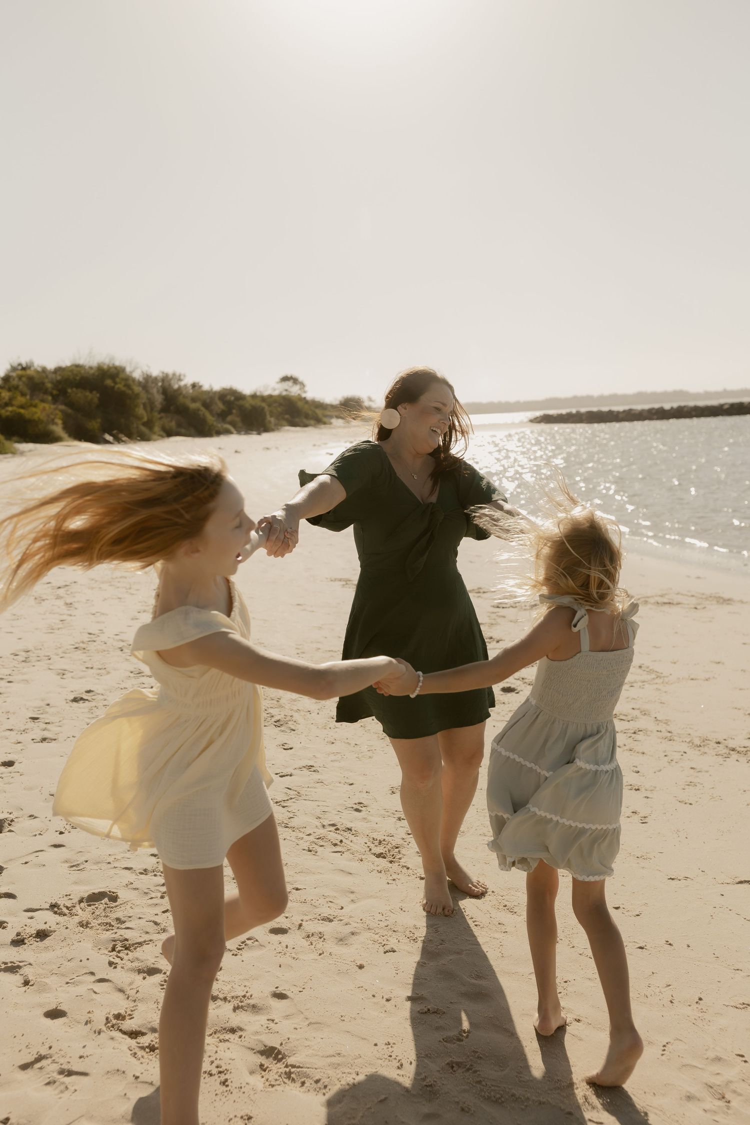 People holding hands and dancing in a circle on a beach during golden hour.