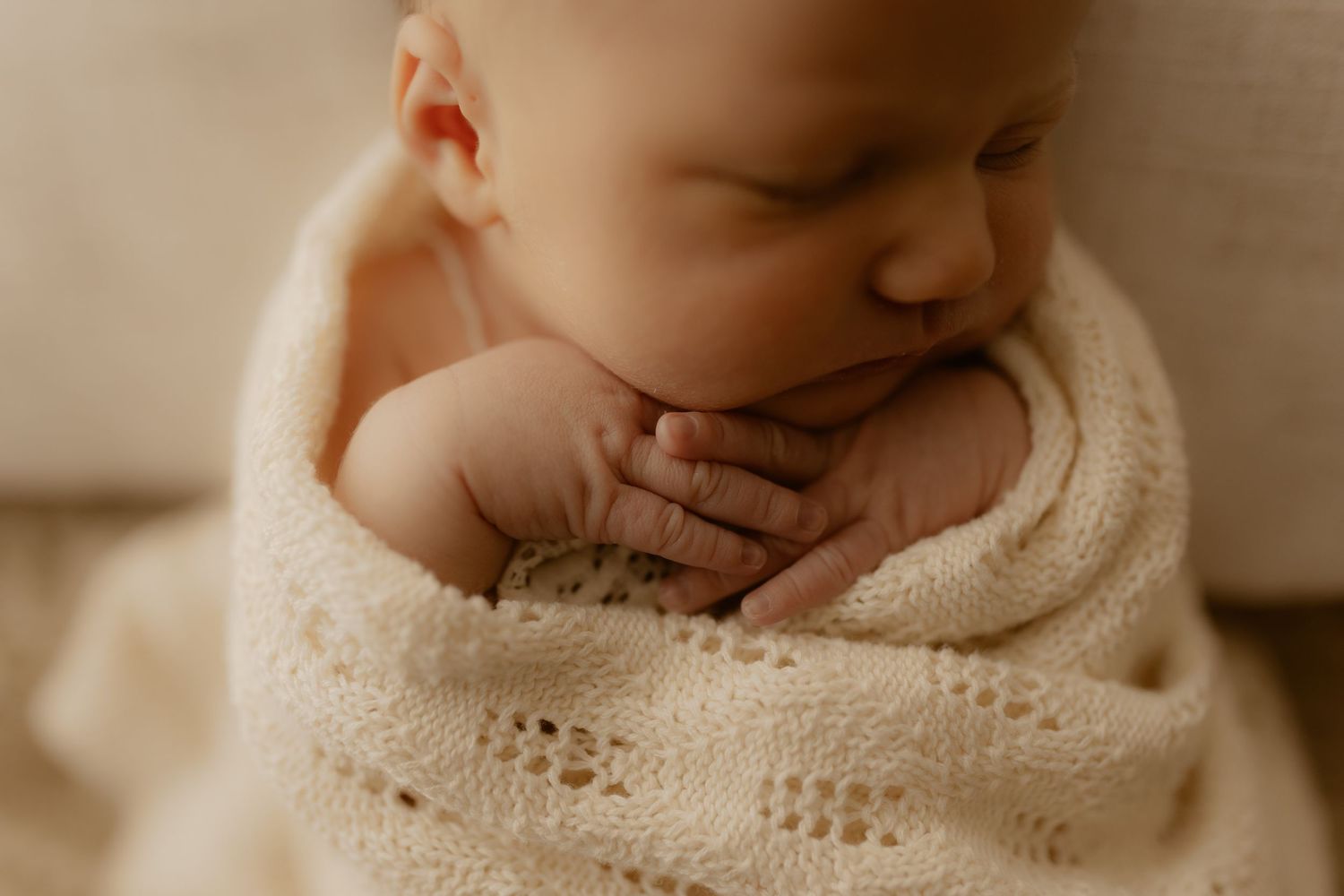Close-up view of sleeping infant wrapped in delicate lace blanket.