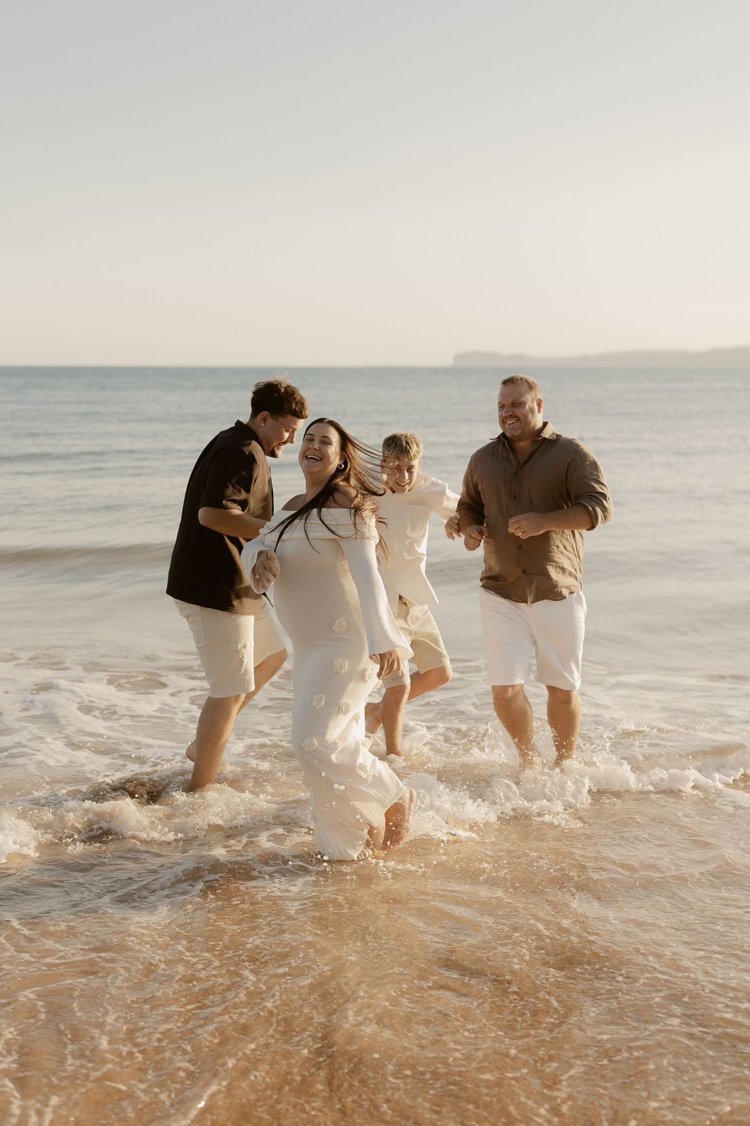 Group of people playing and splashing together in ocean waves at the beach during sunset.