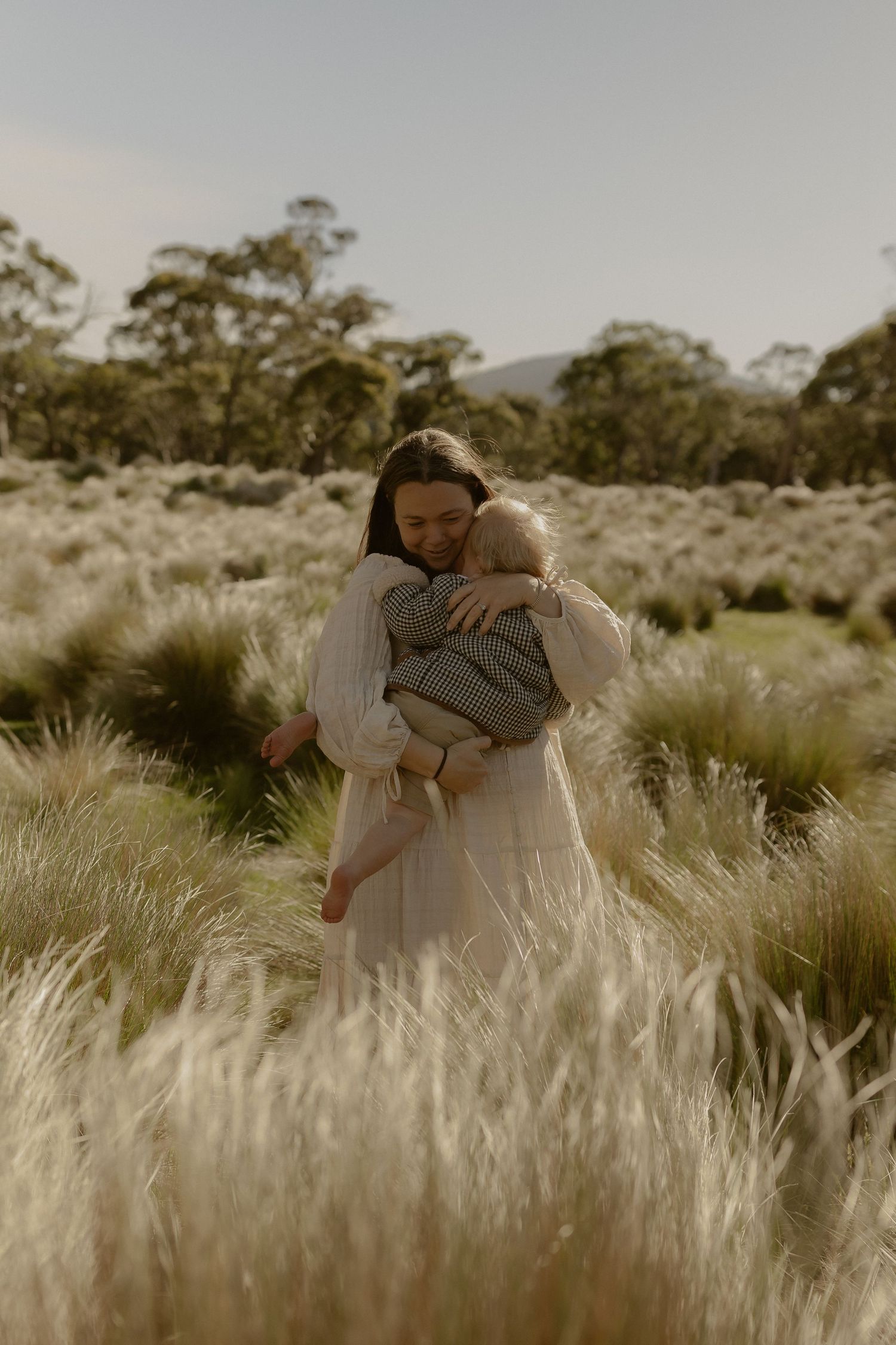 Two people share a tender embrace in a field of tall golden grass during sunset.