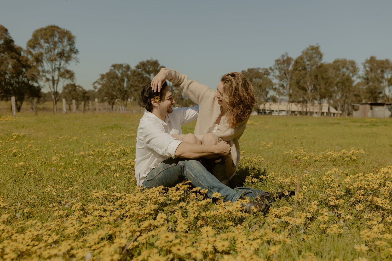 Group of people sitting together in a yellow wildflower field on a sunny afternoon.