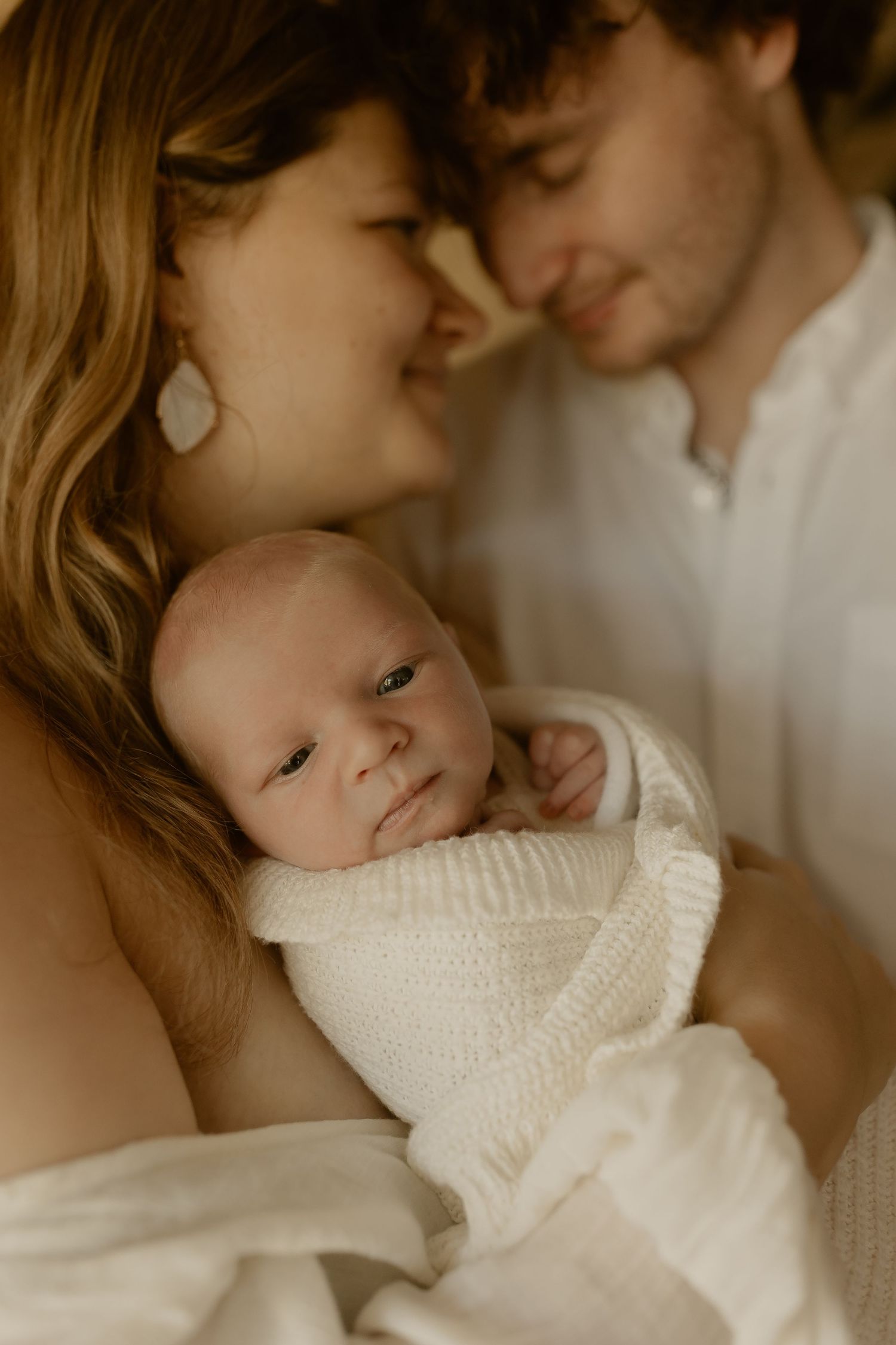 Intimate family portraits in sepia tones featuring a small infant swaddled in cream-colored knit wrap.