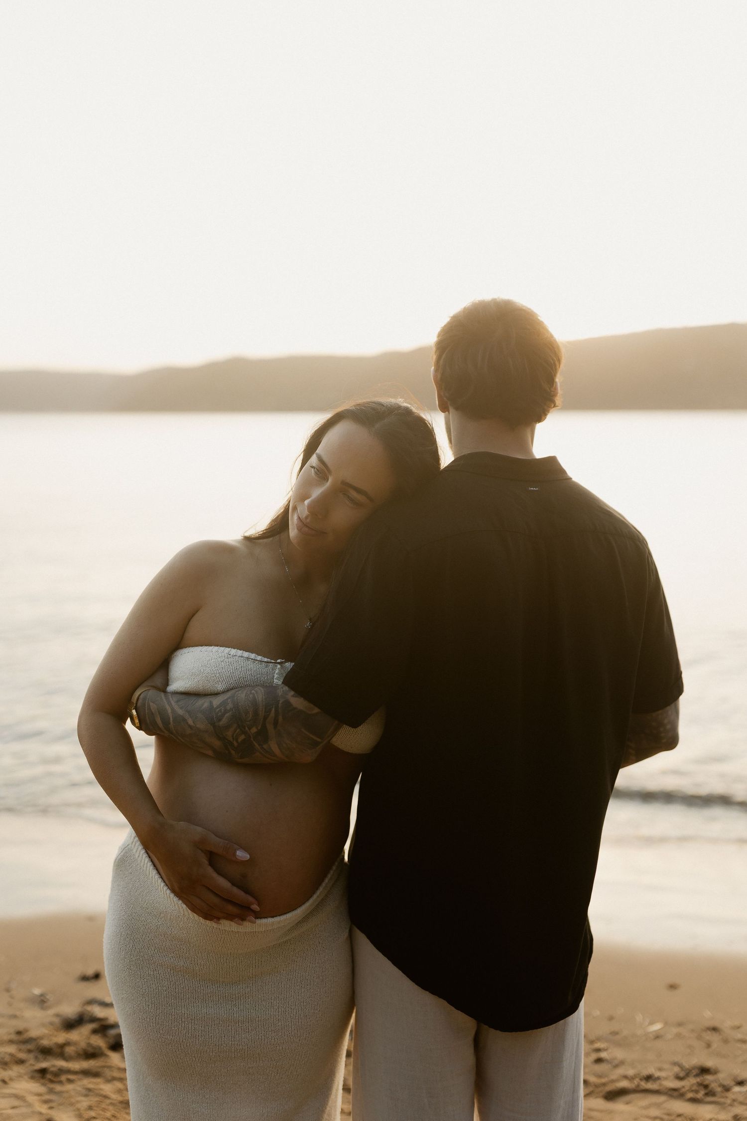 A loving couple embraces on the beach at sunset, silhouetted against the golden ocean waves.