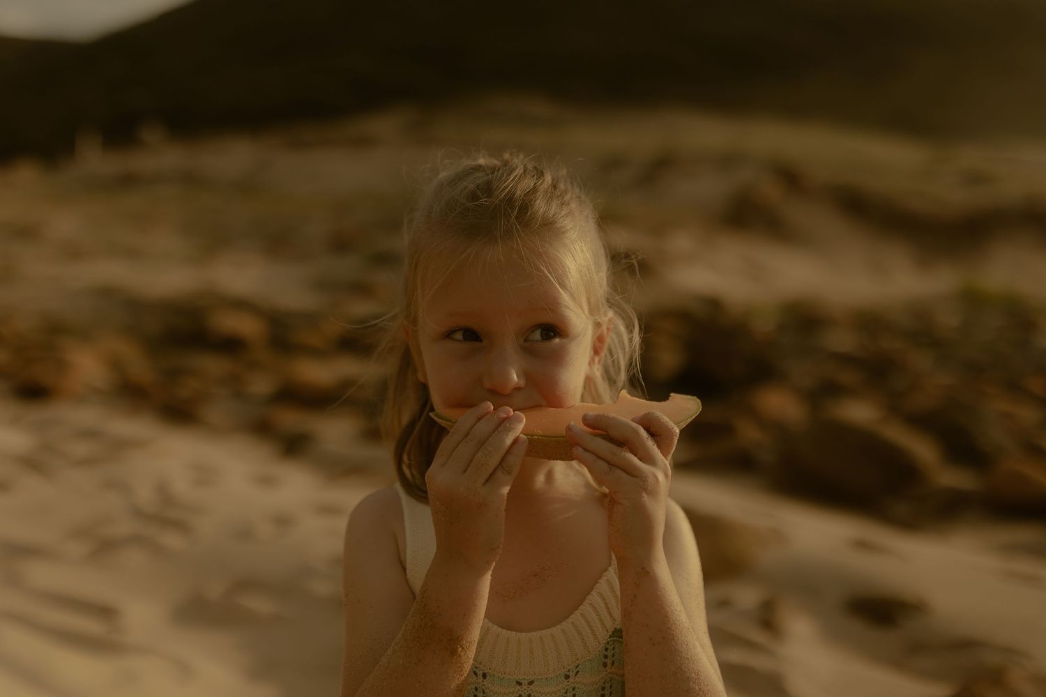 A candid beach portrait captured in warm golden light with coastal cliffs in the background.