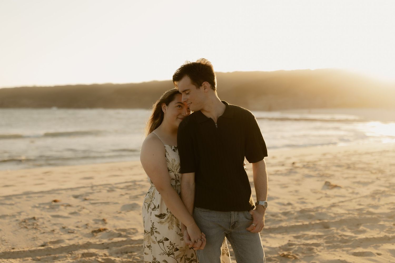 Couple embraces on sandy beach at sunset casting long shadows on the golden shoreline.