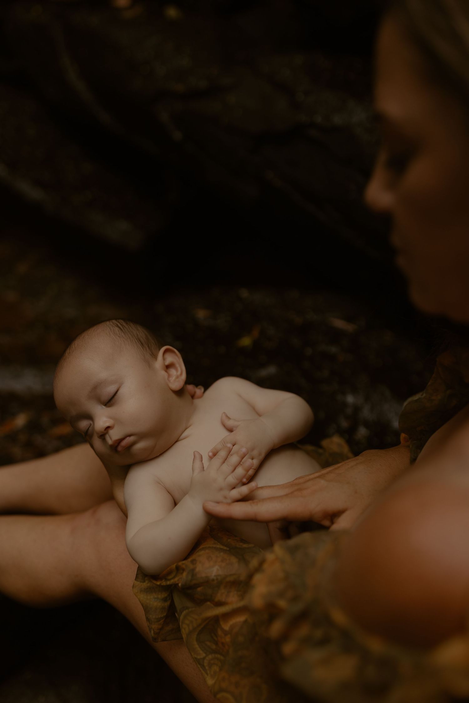 Sleeping baby rests peacefully against mother in atmospheric sepia-toned photograph.