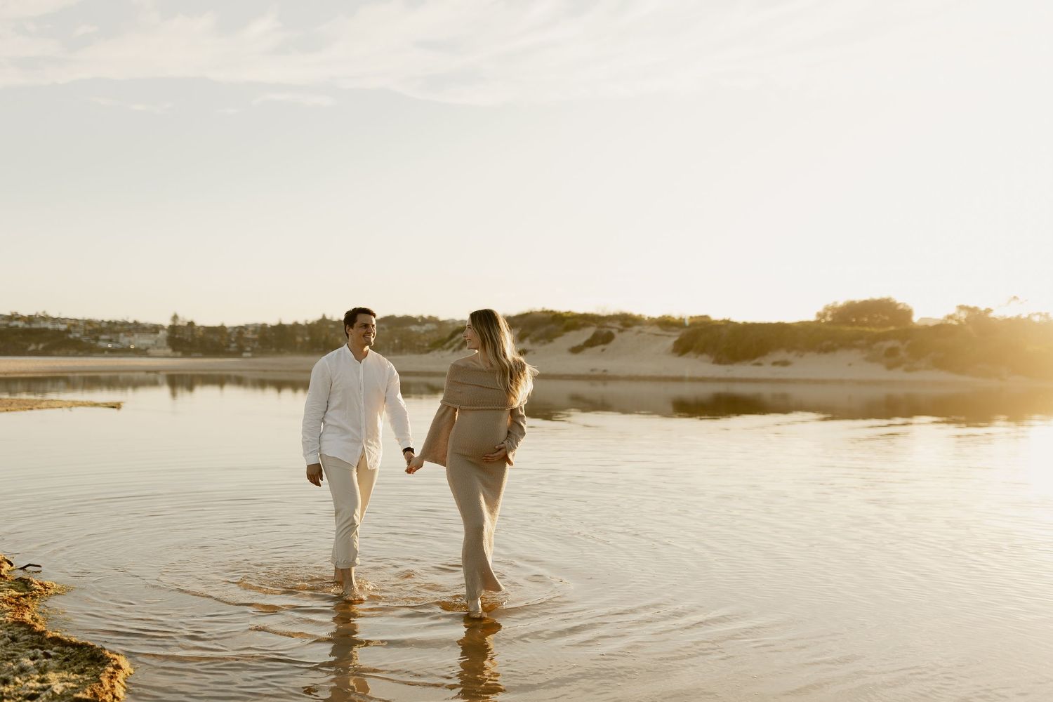 A couple walks hand in hand along a serene beach during golden hour sunset.