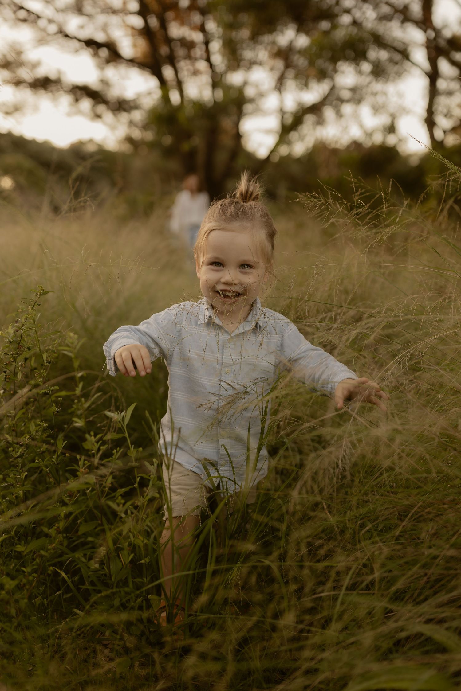 A joyful moment captured in tall grass during golden hour with warm sunlight filtering through the scene.