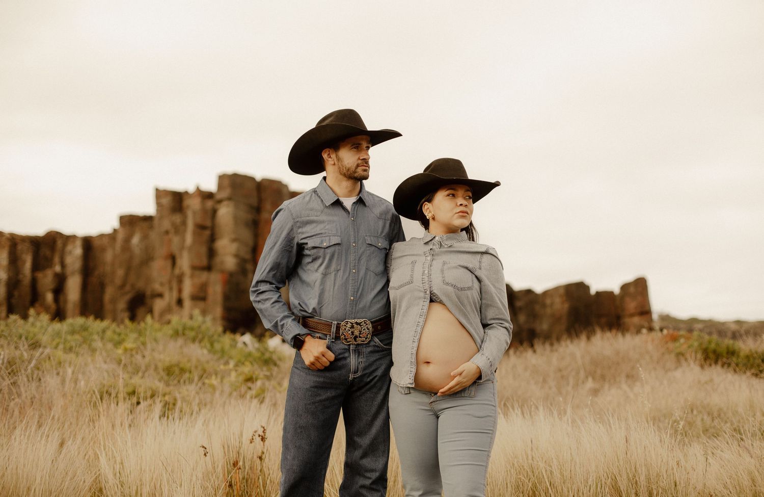 A romantic couple in western attire embraces in a golden wheat field during sunset.