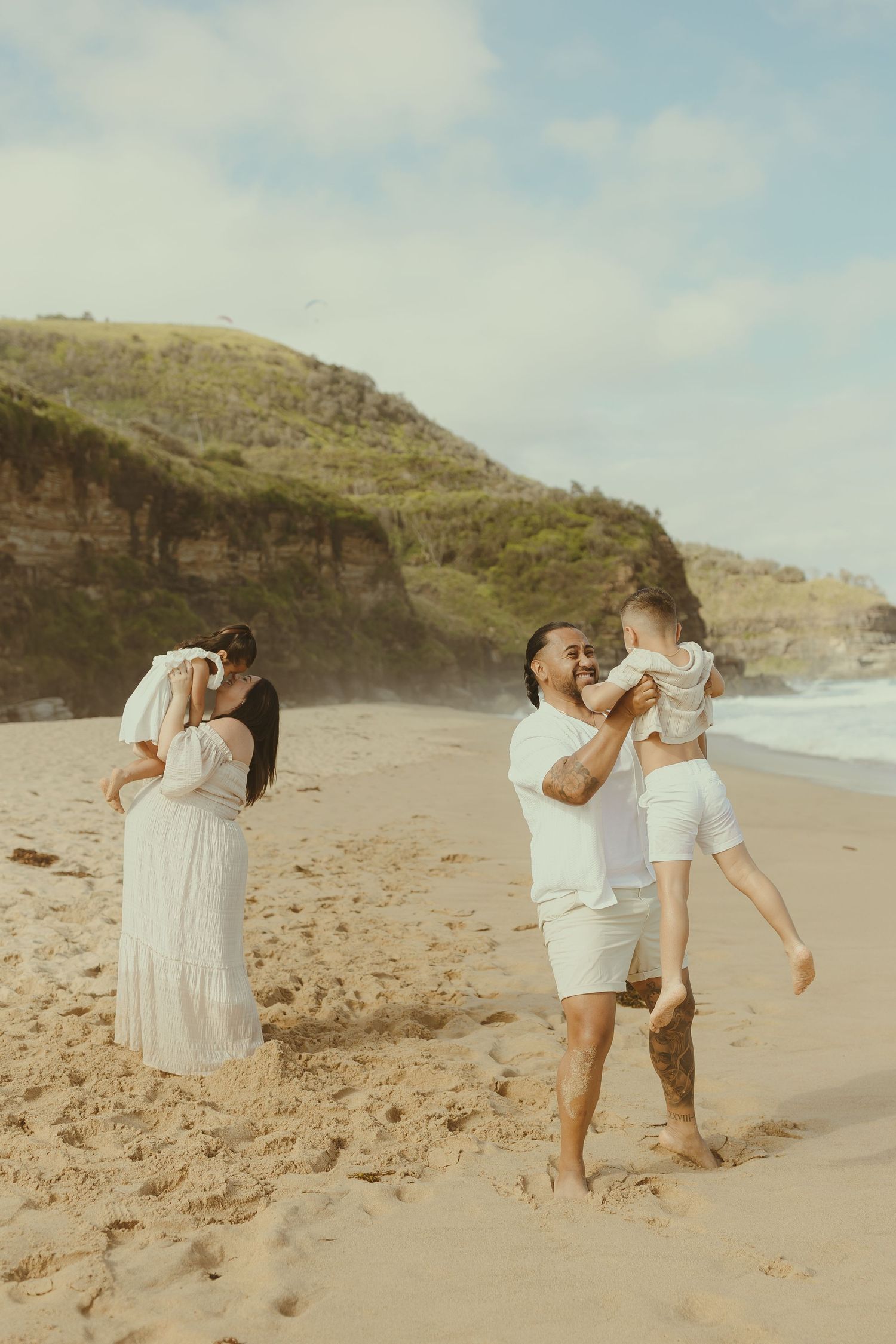 People in white outfits pose and play along a scenic beach with cliffs in the background.