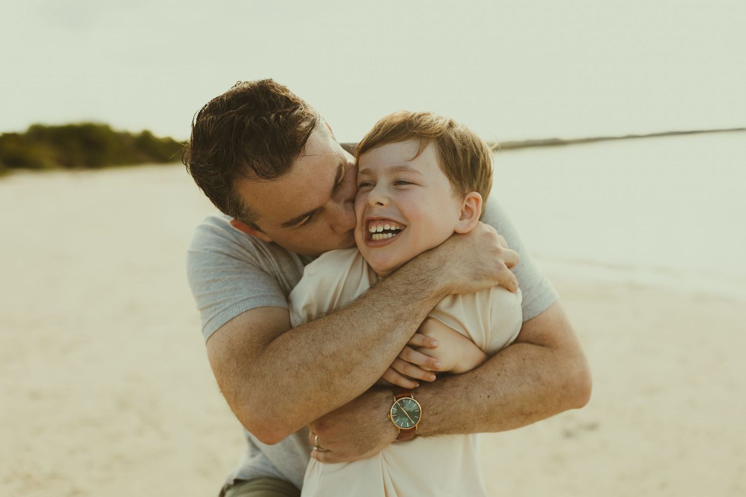 Father and child sharing joyful embraces and laughter in casual beach portraits.