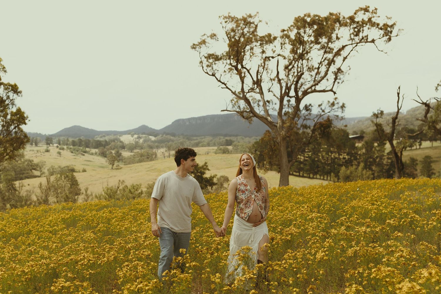 Two people dance together in a vast field of yellow flowers with mountains visible on the horizon.