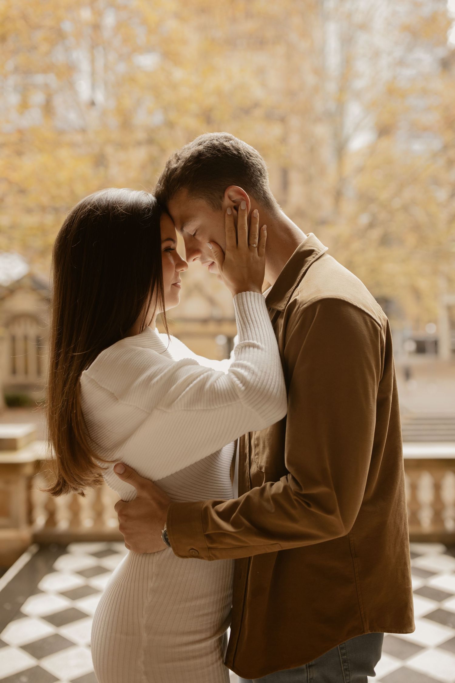 An intimate moment captured between a couple in warm autumn light with classical architecture in the background.