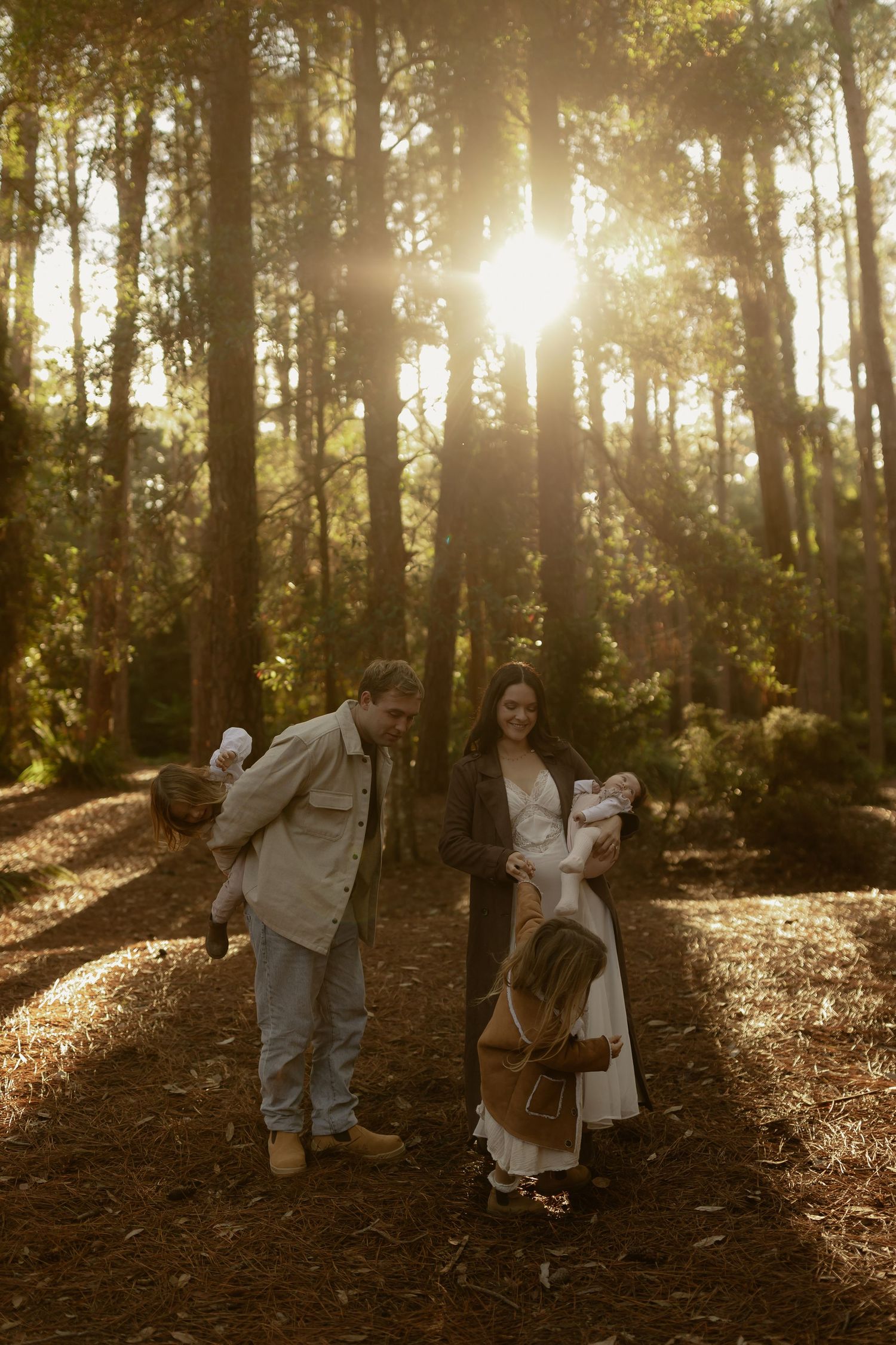 Family of five shares a joyful moment in sunlit pine forest at golden hour.