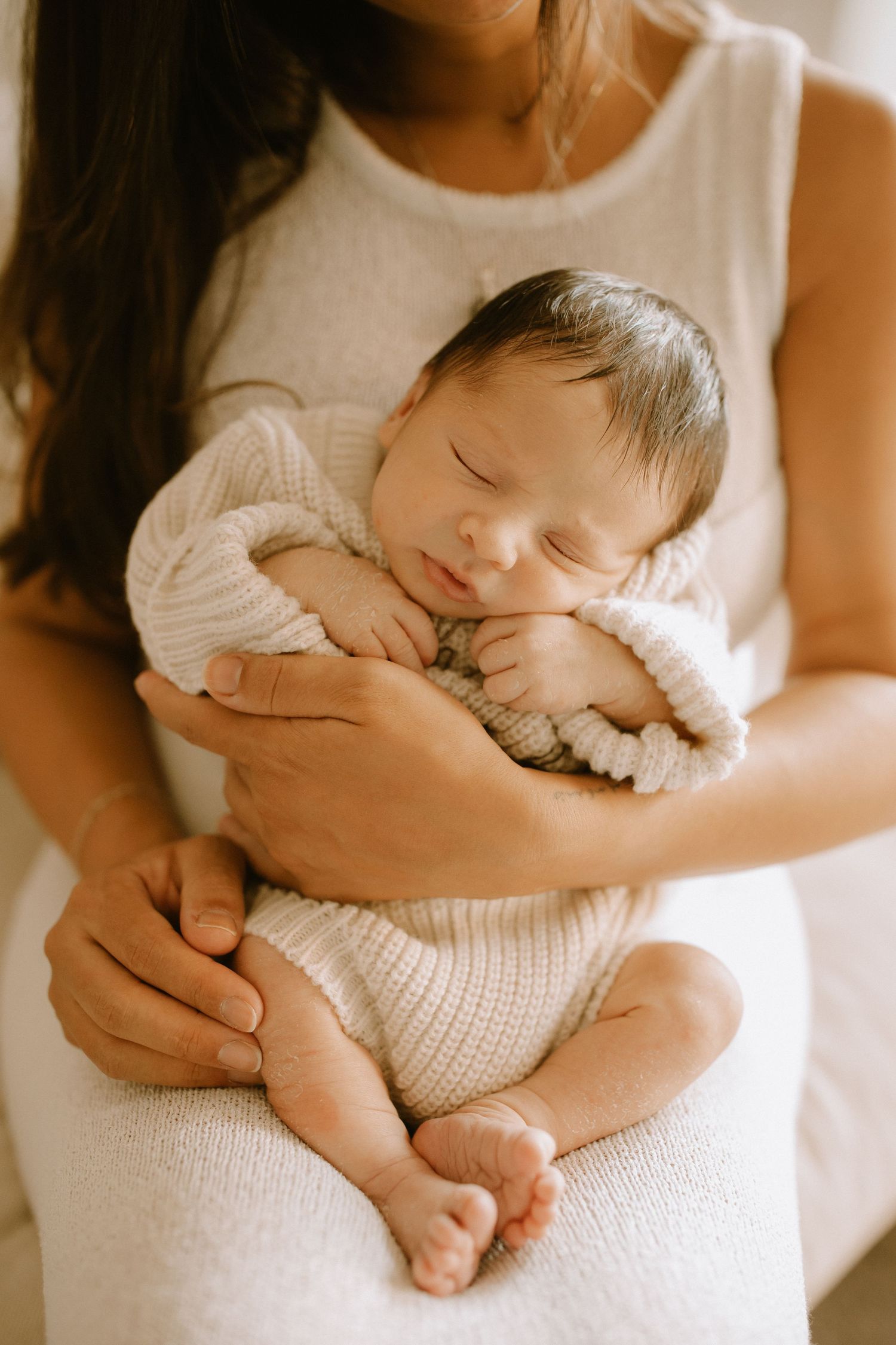 Tender series of newborn baby sleeping peacefully on white blanket while being held close in parent's arms.