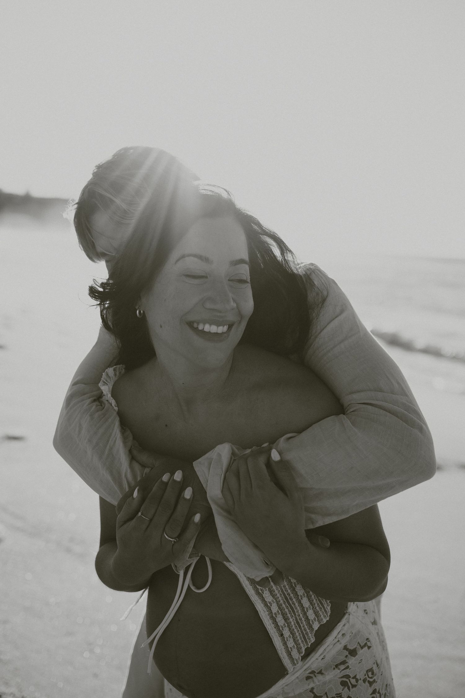A joyful moment captured in black and white as a couple shares laughter on a beach.