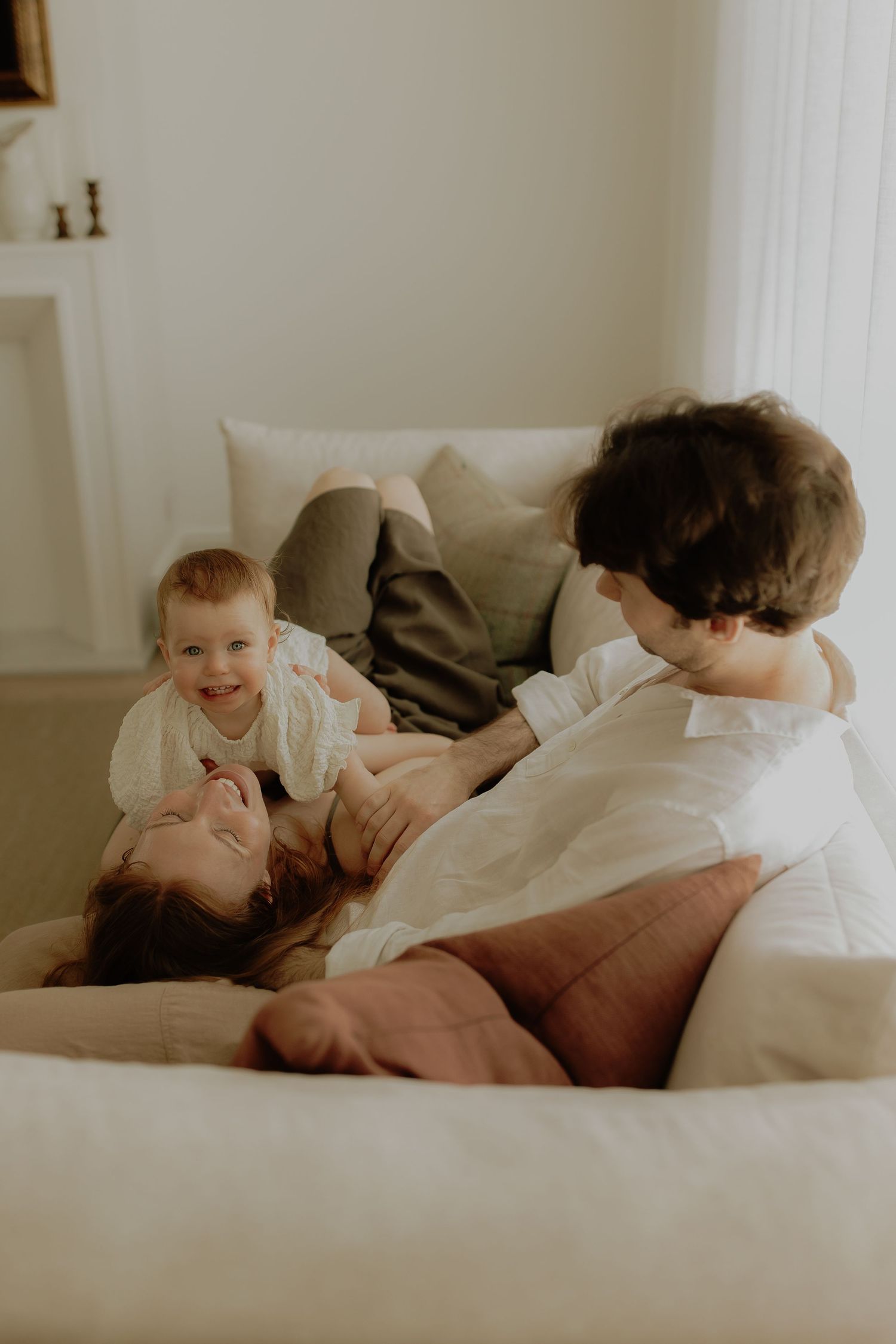 A joyful family relaxing on a cozy sofa, with a laughing baby and two adults sharing a warm moment.